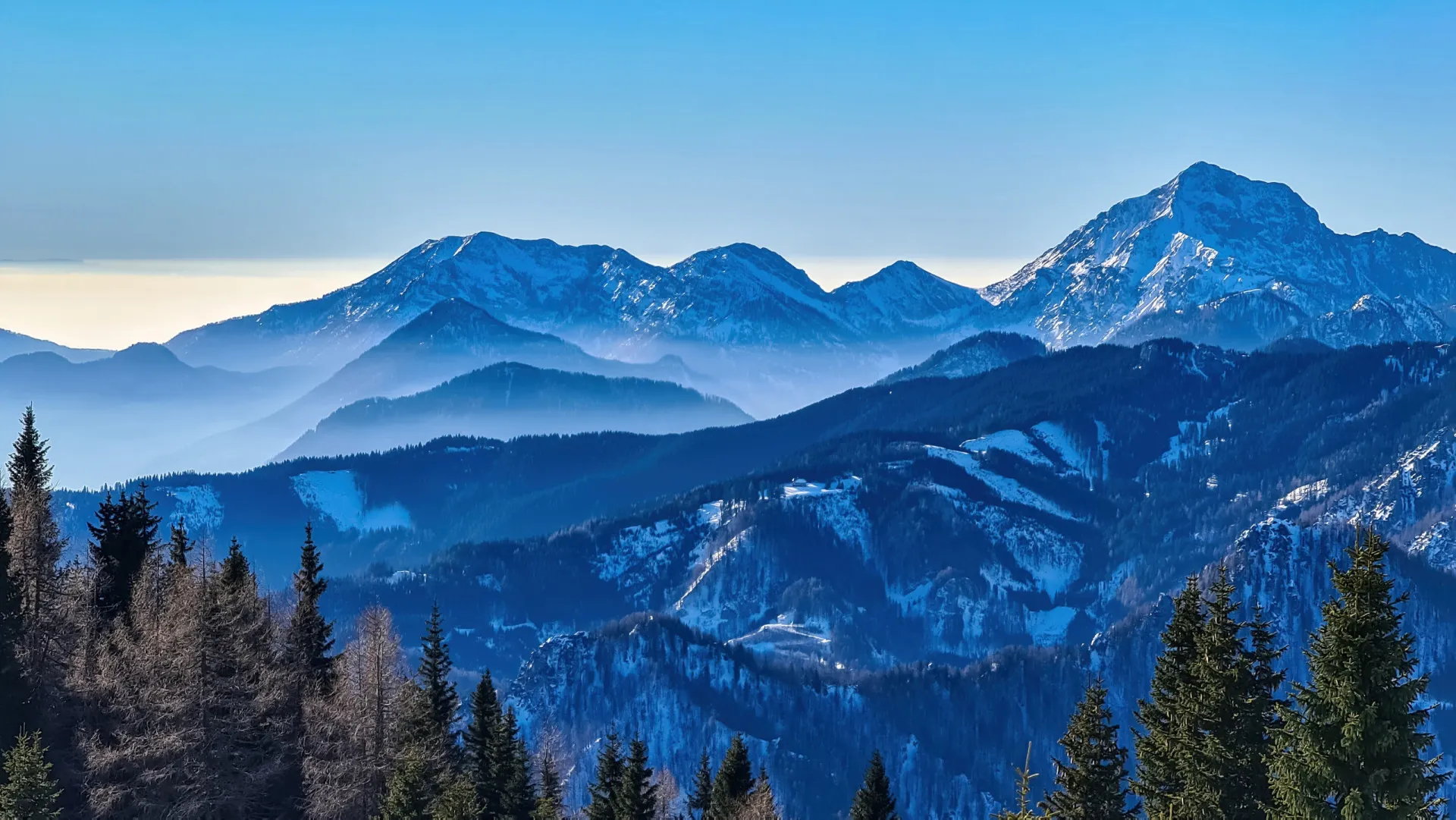 Paisagem majestosa dos Alpes austríacos, com montanhas cobertas de neve sob um céu azul.