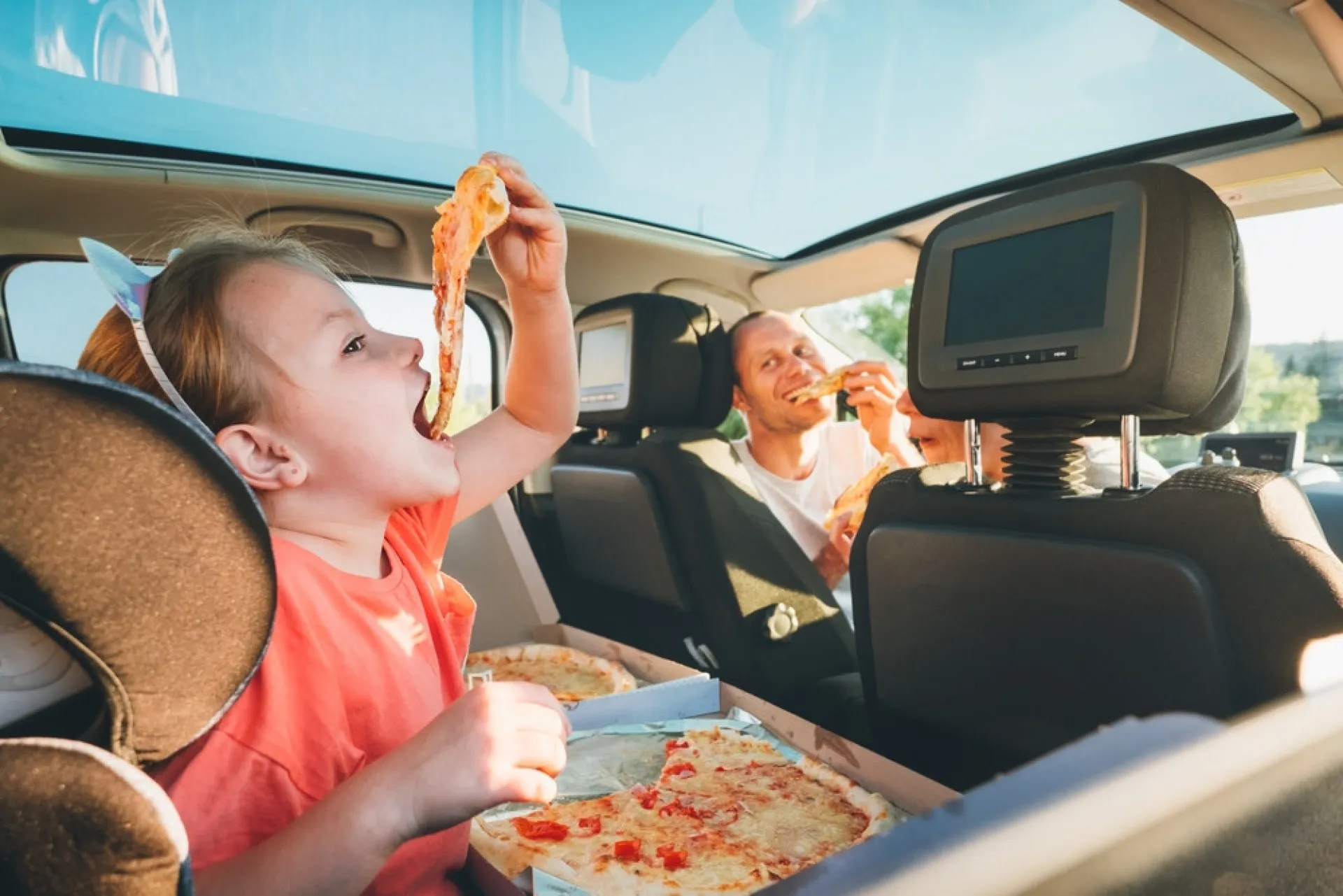 Uma criança comendo batatas fritas no banco de trás de um carro, enquanto os pais dirigem.