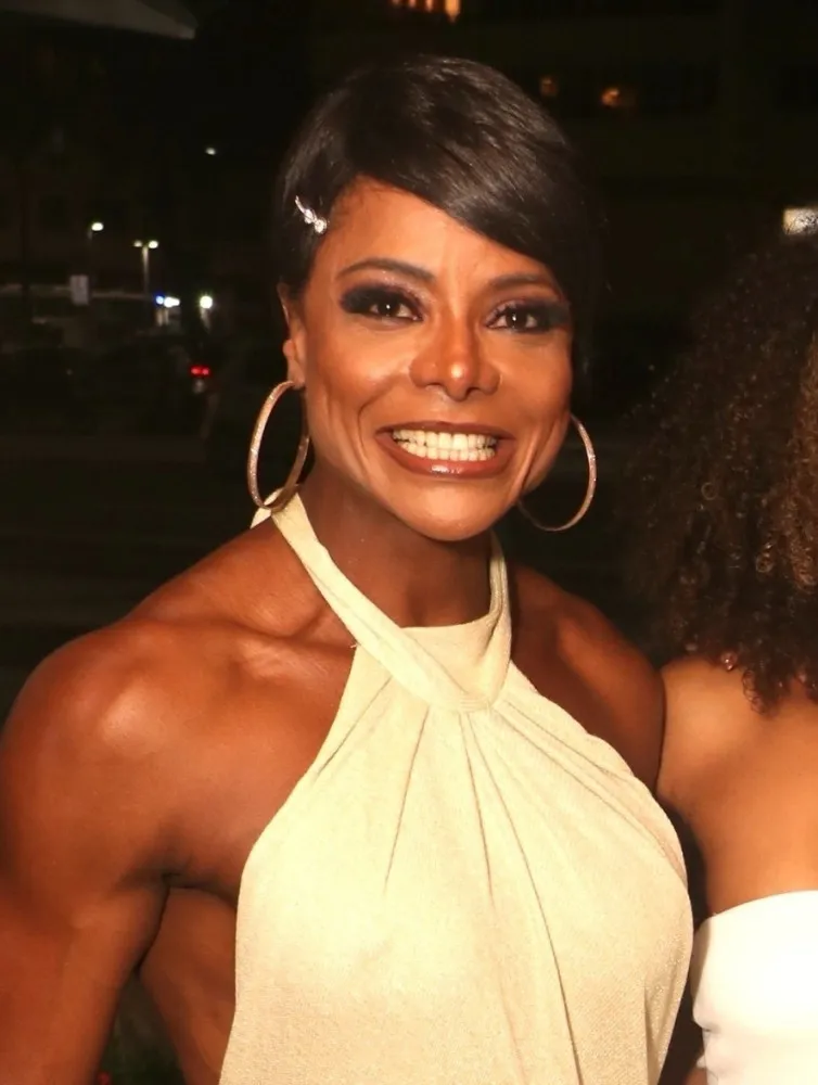 Adriana Bombom sorrindo para a câmera em um evento, mostrando sua boa forma.