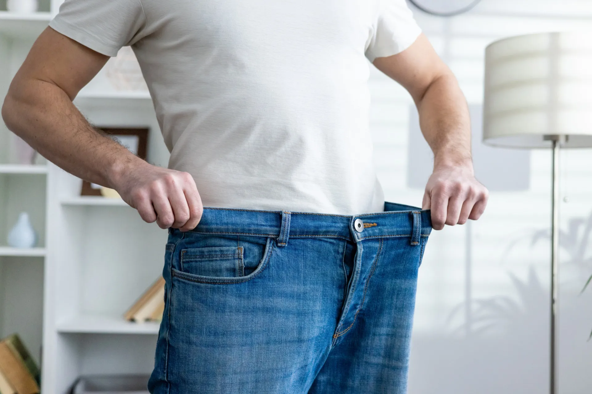 Uma pessoa segurando uma calça jeans antiga que agora está muito larga, mostrando a perda de peso real.