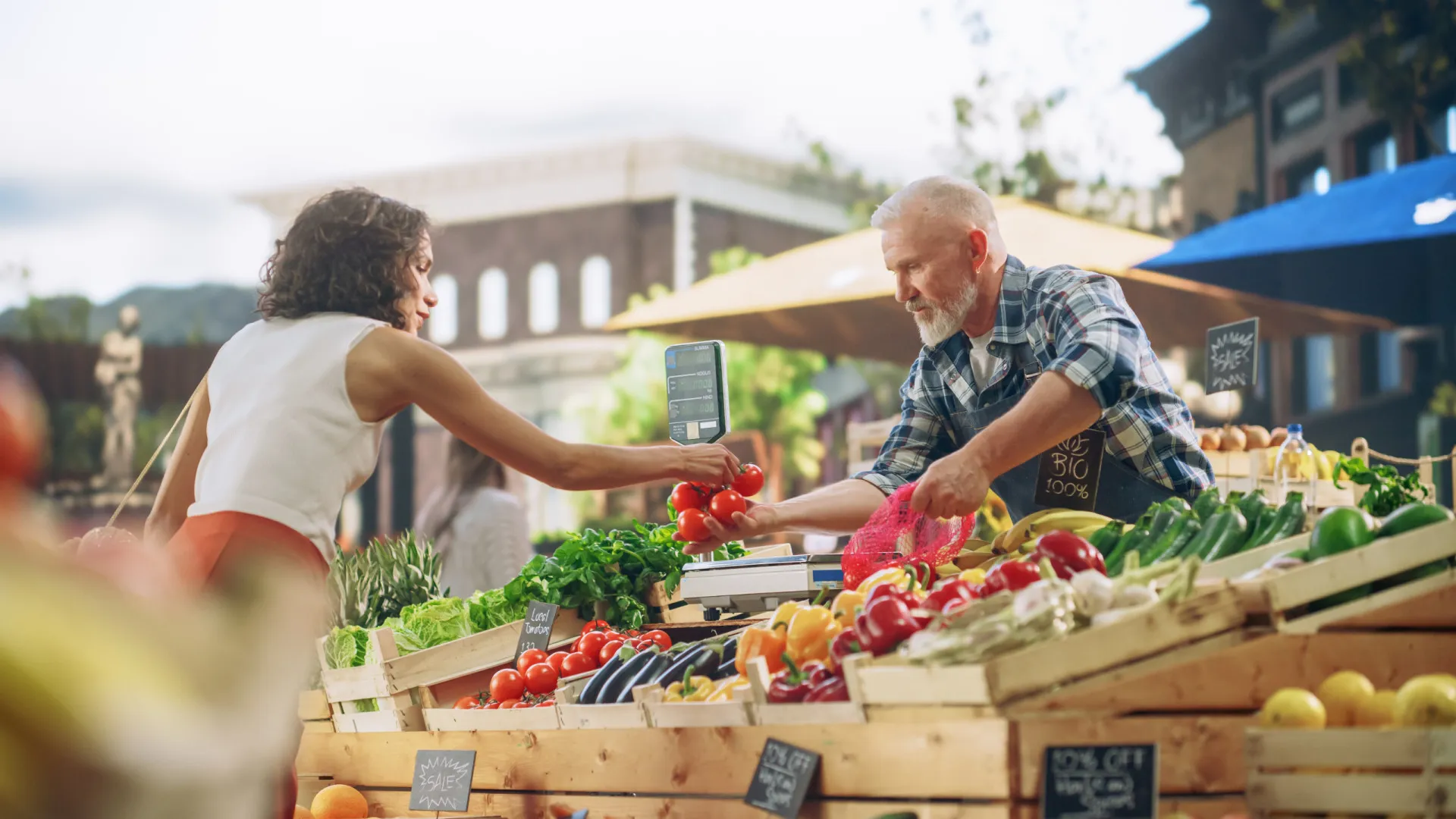 Uma pessoa sorrindo em um mercado de agricultores, cercada por frutas e vegetais frescos e coloridos.