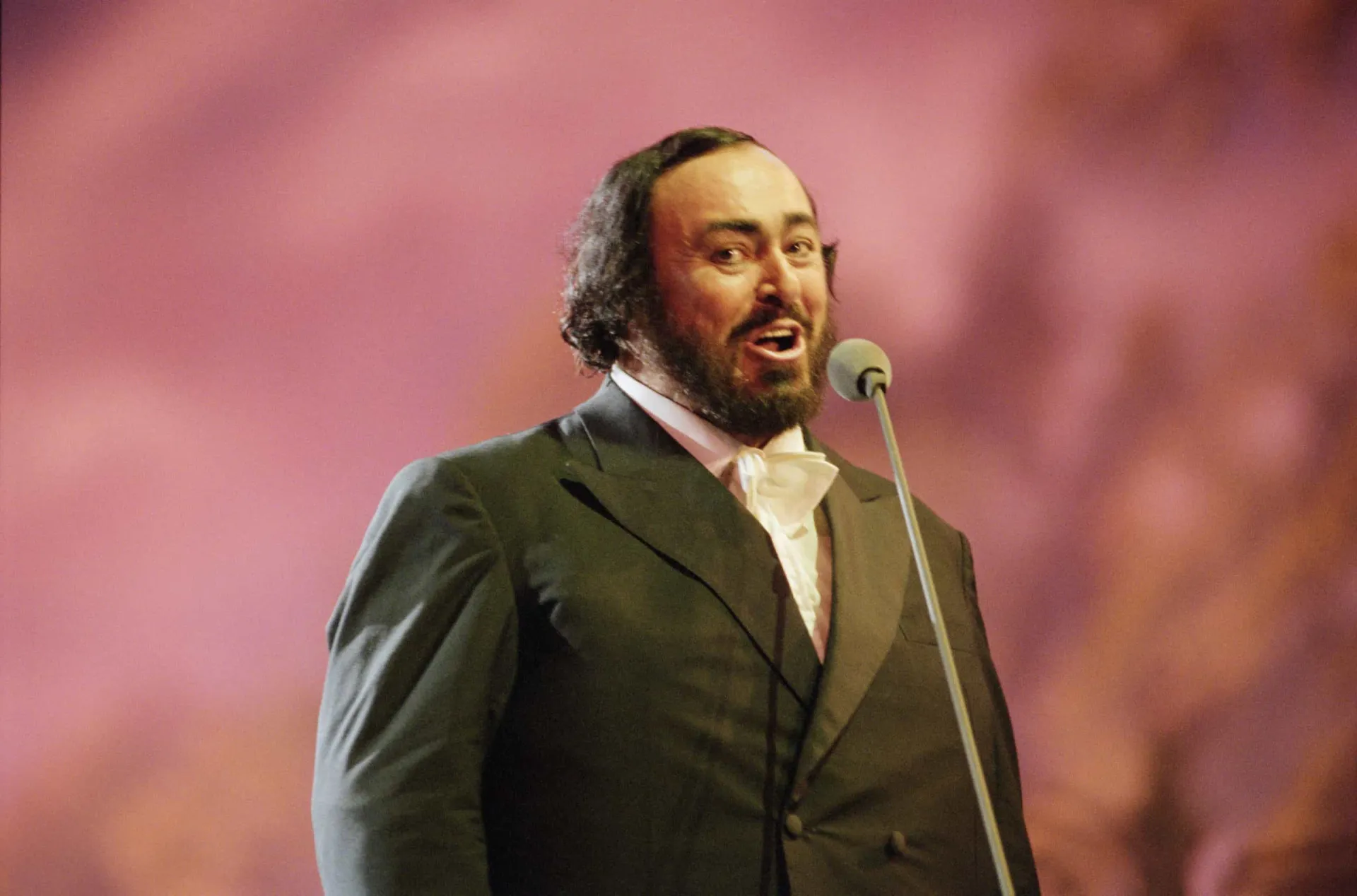 O tenor de ópera italiano Luciano Pavarotti cantando apaixonadamente no palco.