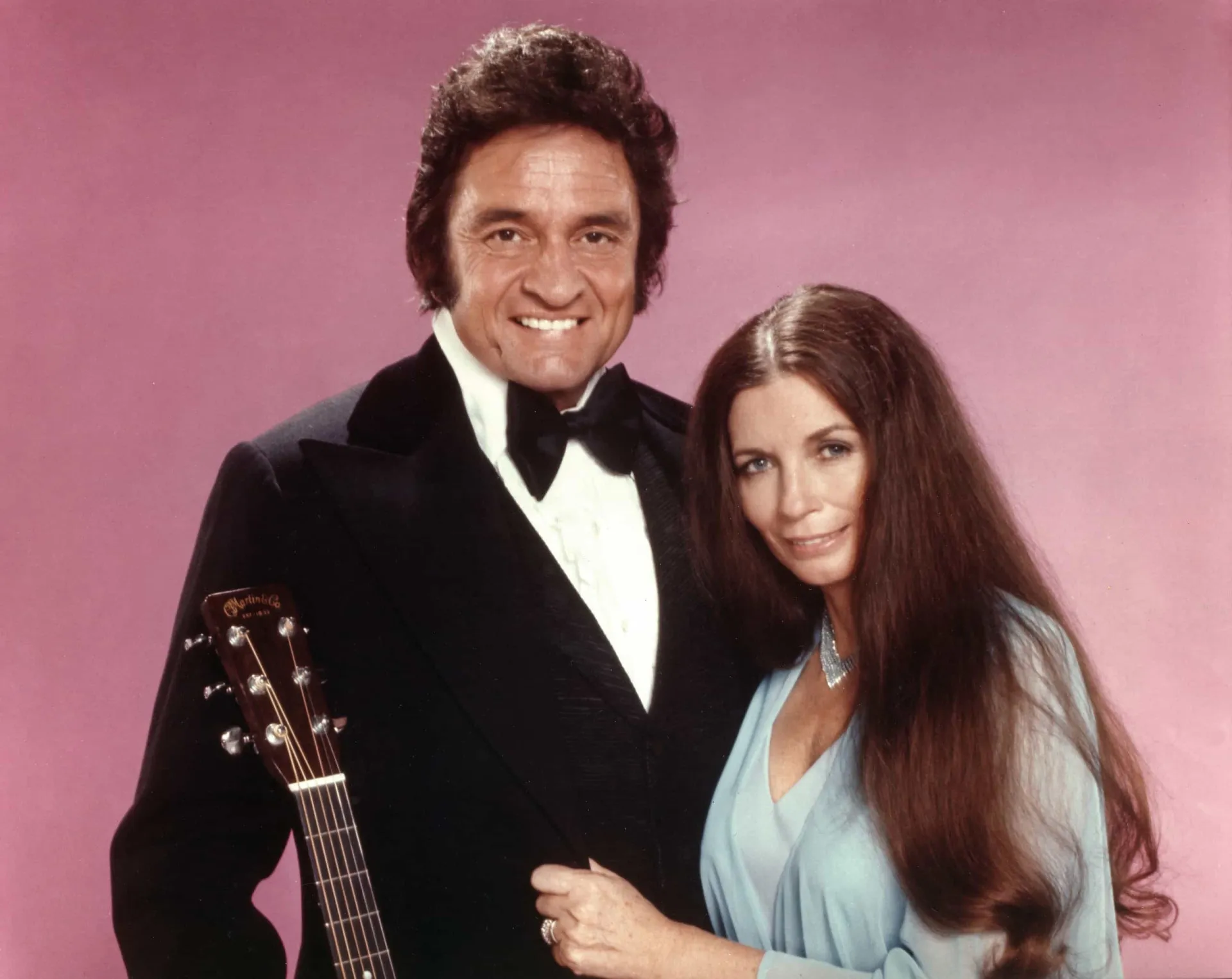 Johnny Cash e June Carter Cash se apresentando juntos no palco, com olhares de admiração mútua.