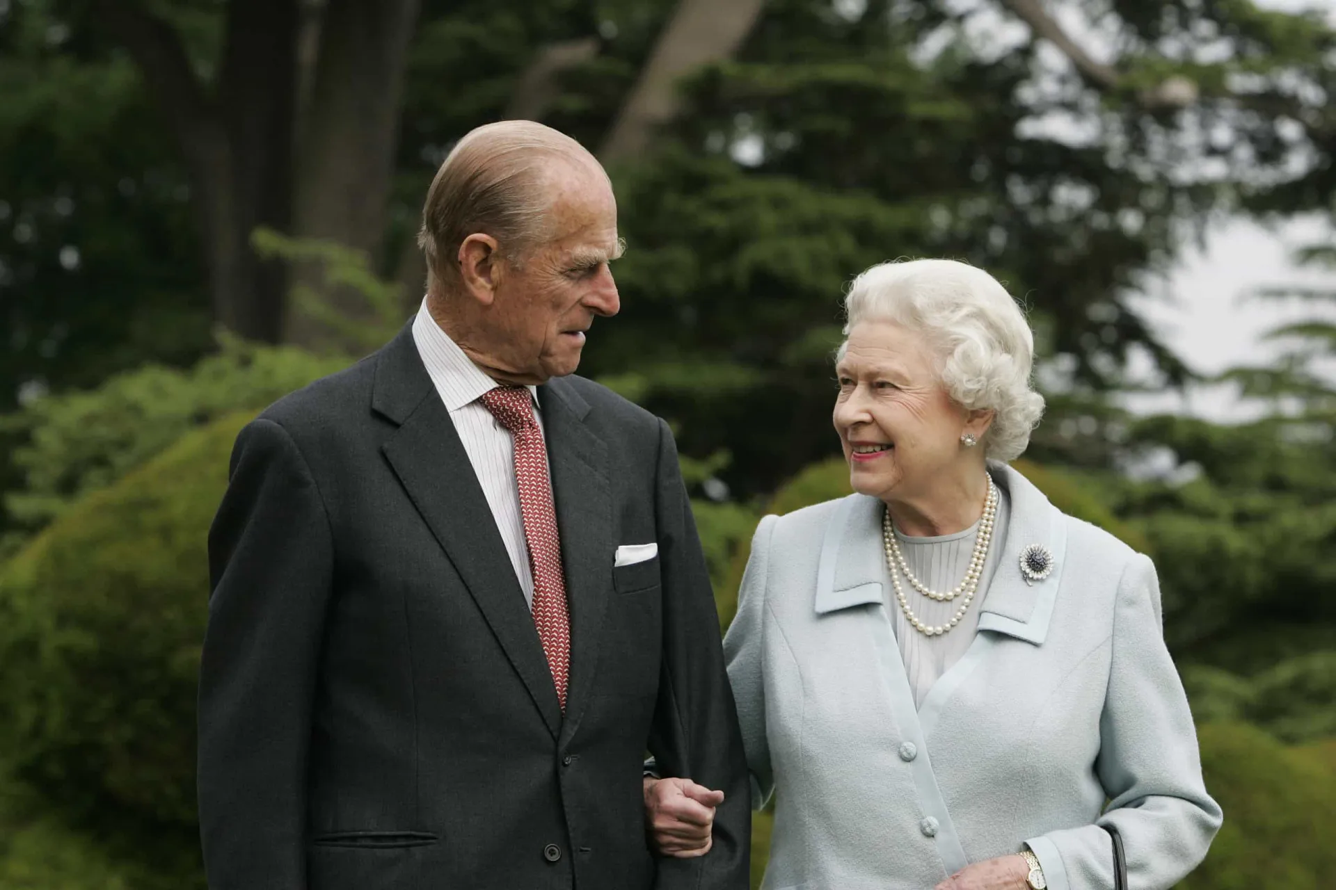 A Rainha Elizabeth II e o Príncipe Philip sorrindo um para o outro durante um evento oficial.