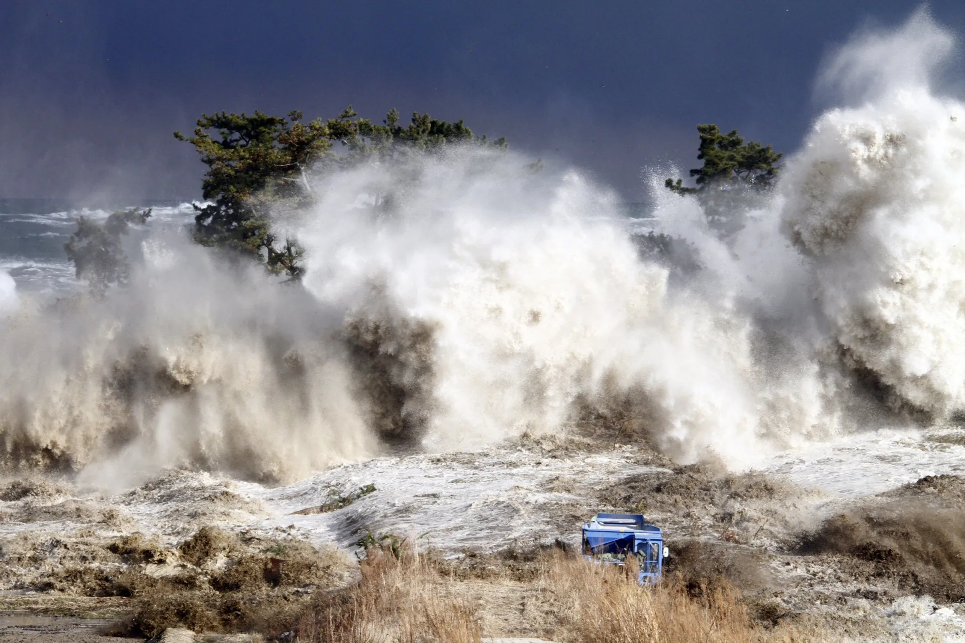 Foto aérea mostrando a devastação causada pelo tsunami de 2011 no Japão, com destroços e inundações.