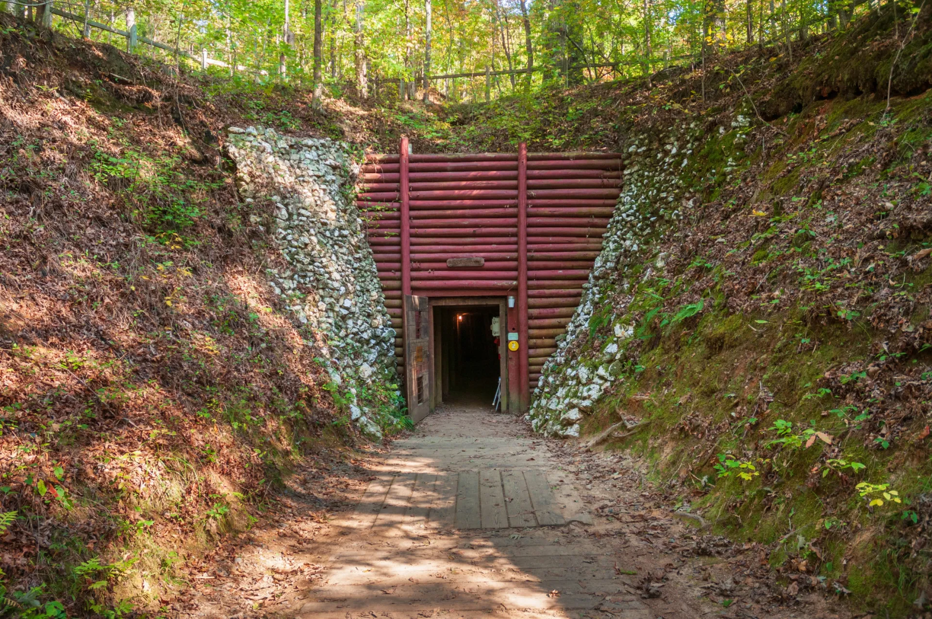 Entrada de uma antiga mina de ouro com trilhos de carrinho e estrutura de madeira.