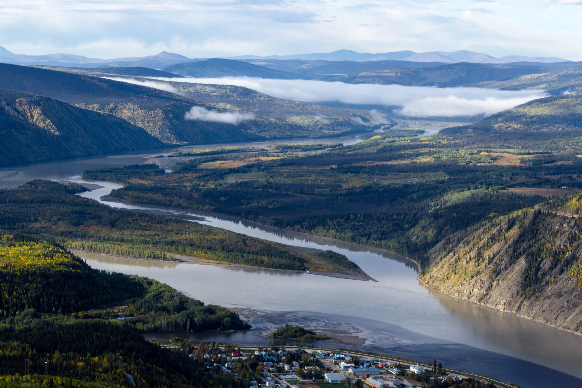Paisagem do Yukon com o Rio Klondike e cabanas de madeira históricas nas margens.