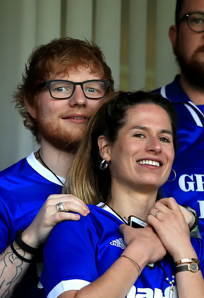 Ed Sheeran e Cherry Seaborn posando juntos em um campo de futebol.