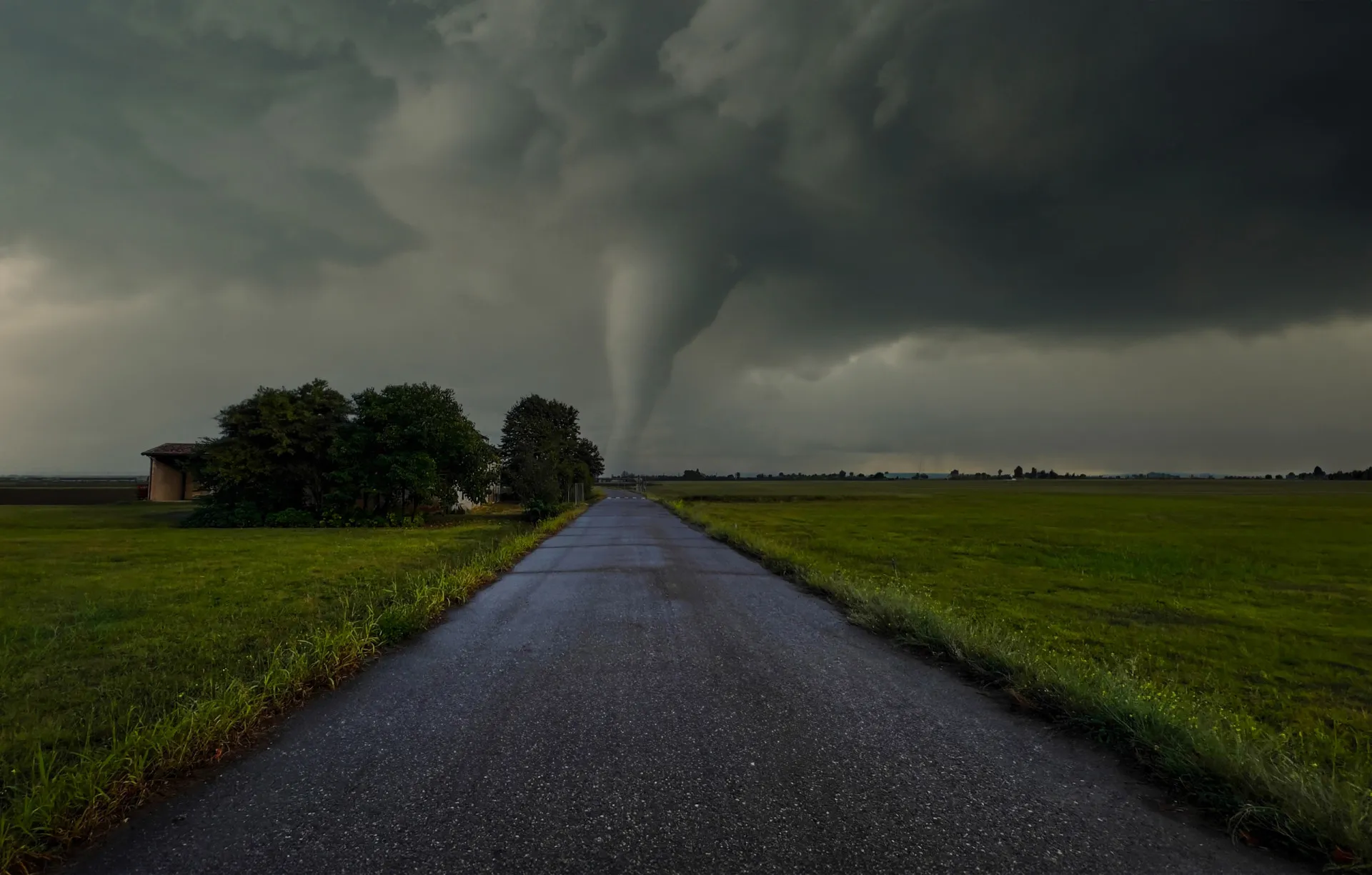 Um tornado massivo se movendo por um campo, com um funil de nuvens tocando o solo.