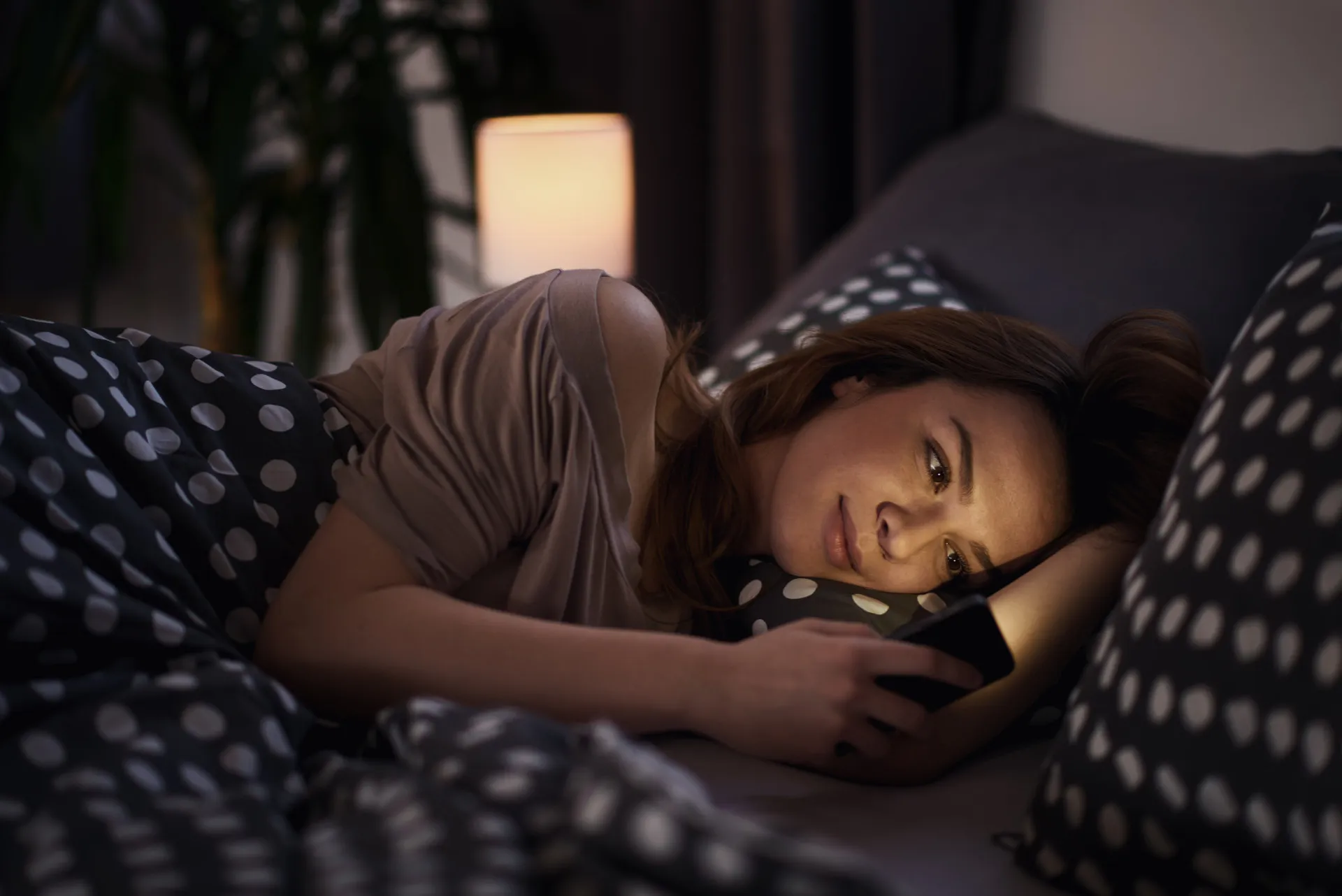 Mulher na cama olhando para o celular à noite, ilustrando um mau hábito de sono.