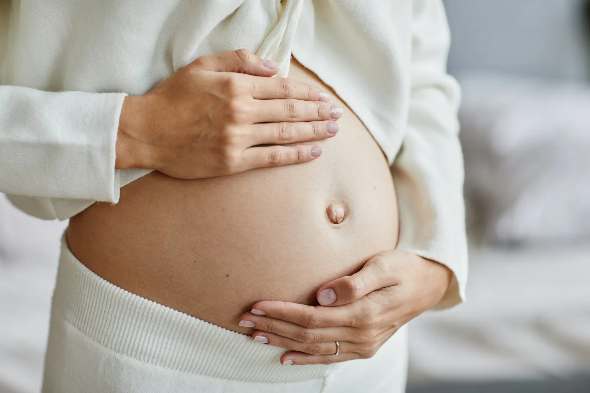 Mulher de perfil, com as mãos na barriga, que parece estar inchada.