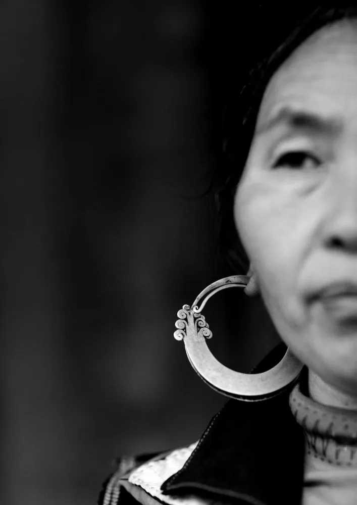 Close de uma mulher Hmong sorrindo e exibindo seus brincos de argola ornamentados.