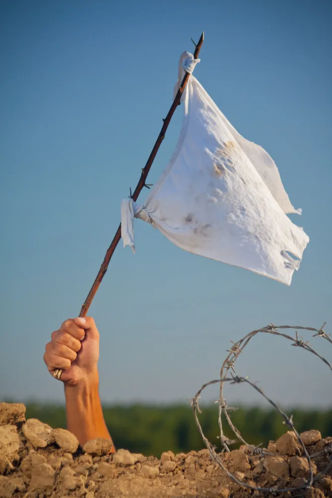 Uma mão segurando uma pequena bandeira branca tremulando ao vento.