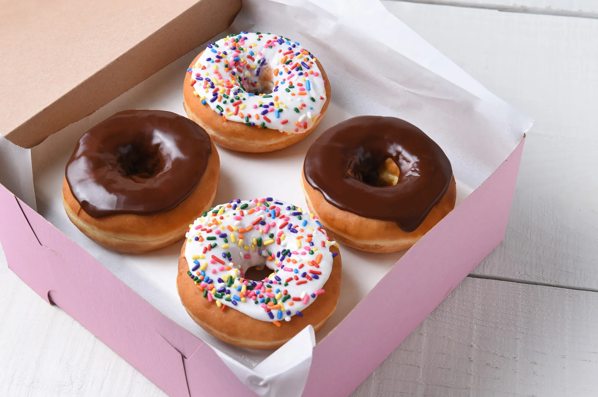 Uma caixa de donuts rosa aberta, revelando uma variedade de rosquinhas coloridas.