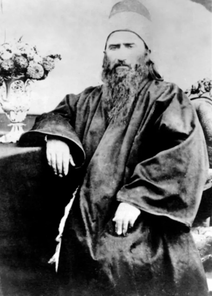 Retrato fotográfico de Bahá'u'lláh, o fundador da Fé Bahá'í, com um olhar sereno e turbante.