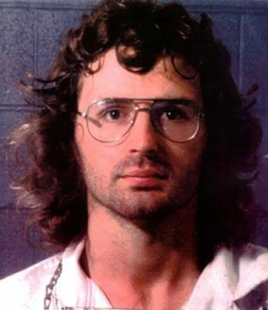 Retrato de David Koresh, líder do culto Ramo Davidiano, usando óculos e com uma expressão séria.