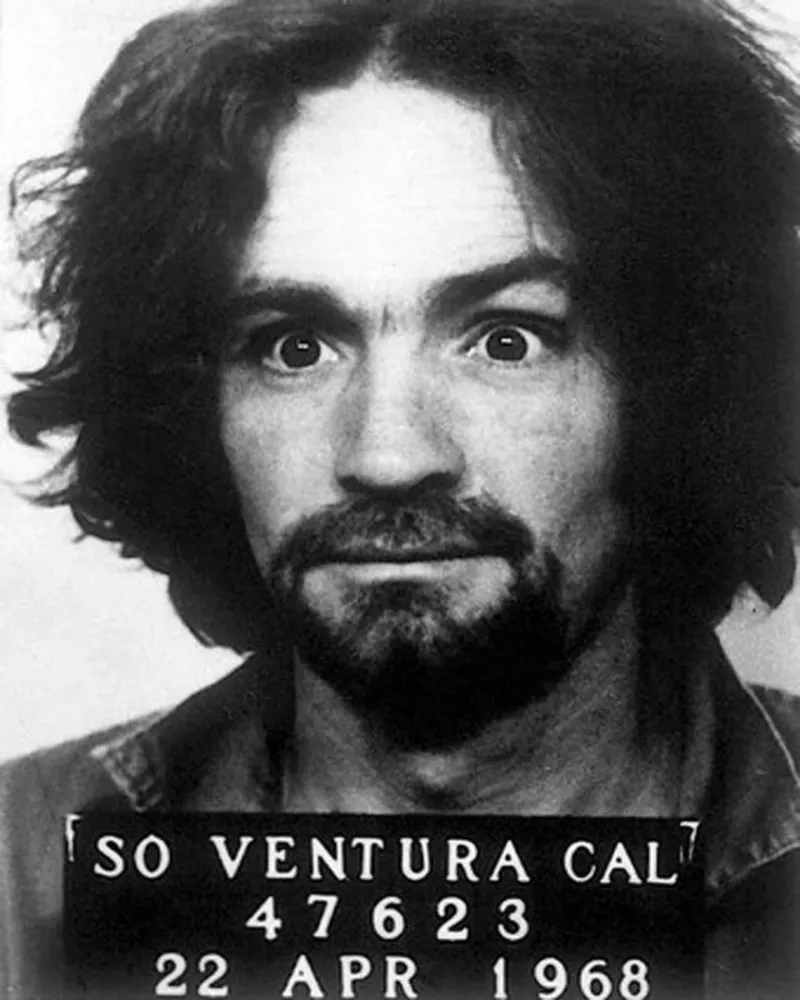 Charles Manson em uma fotografia policial, com cabelo longo, barba e um olhar selvagem e penetrante.