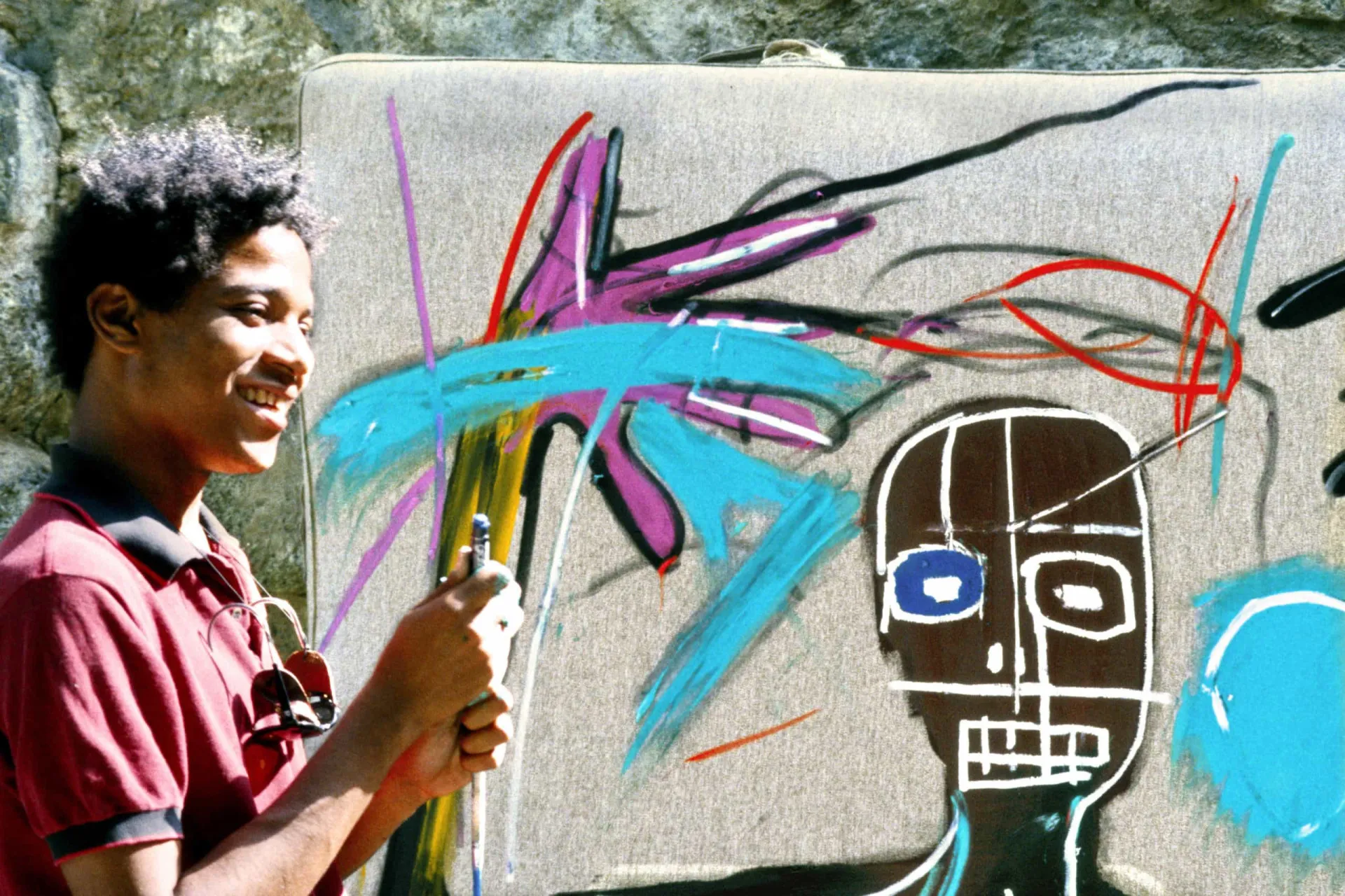 O artista Jean-Michel Basquiat em seu estúdio, cercado por suas obras de arte vibrantes.