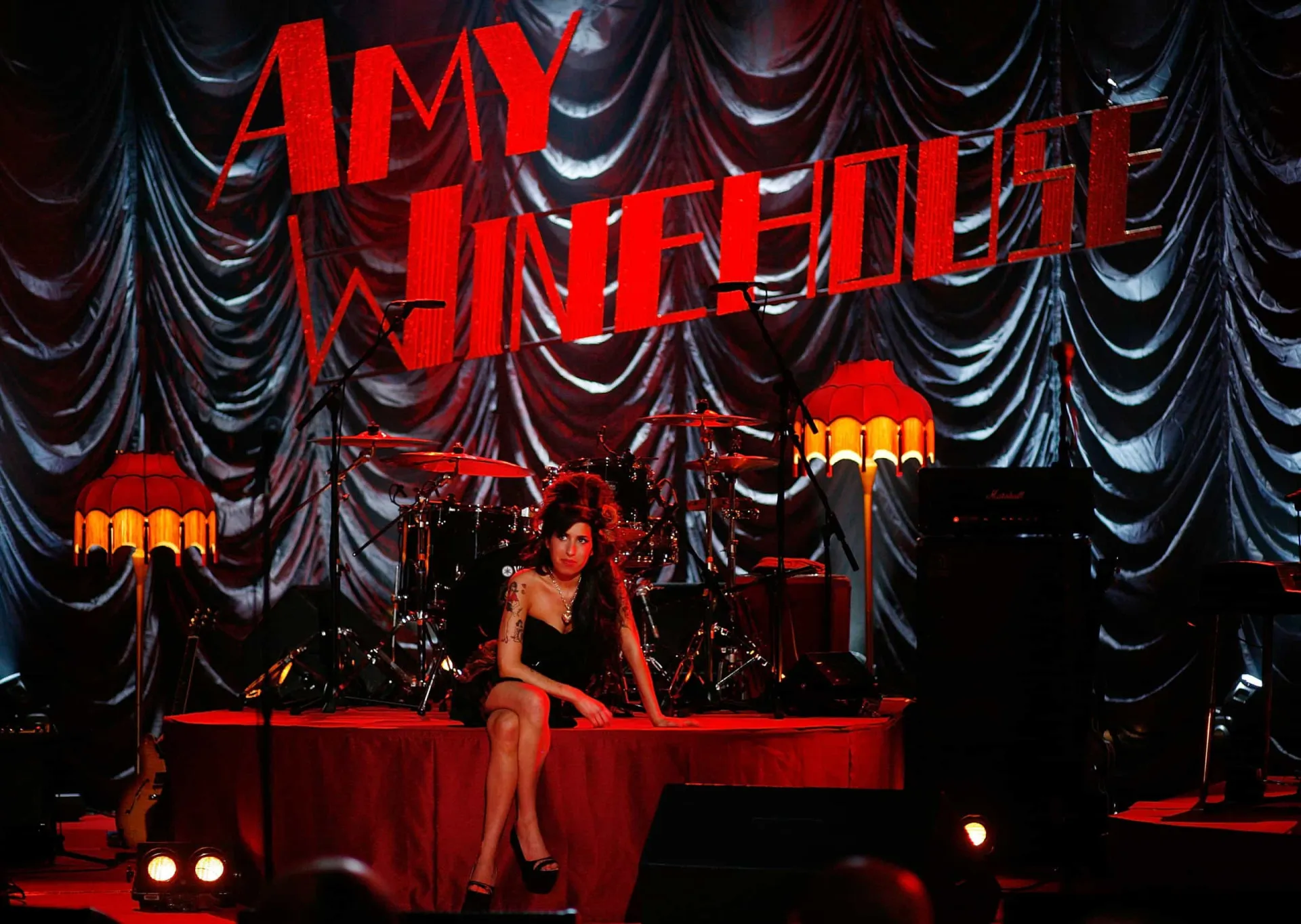Amy Winehouse com seu característico penteado beehive e delineador, olhando para o lado.