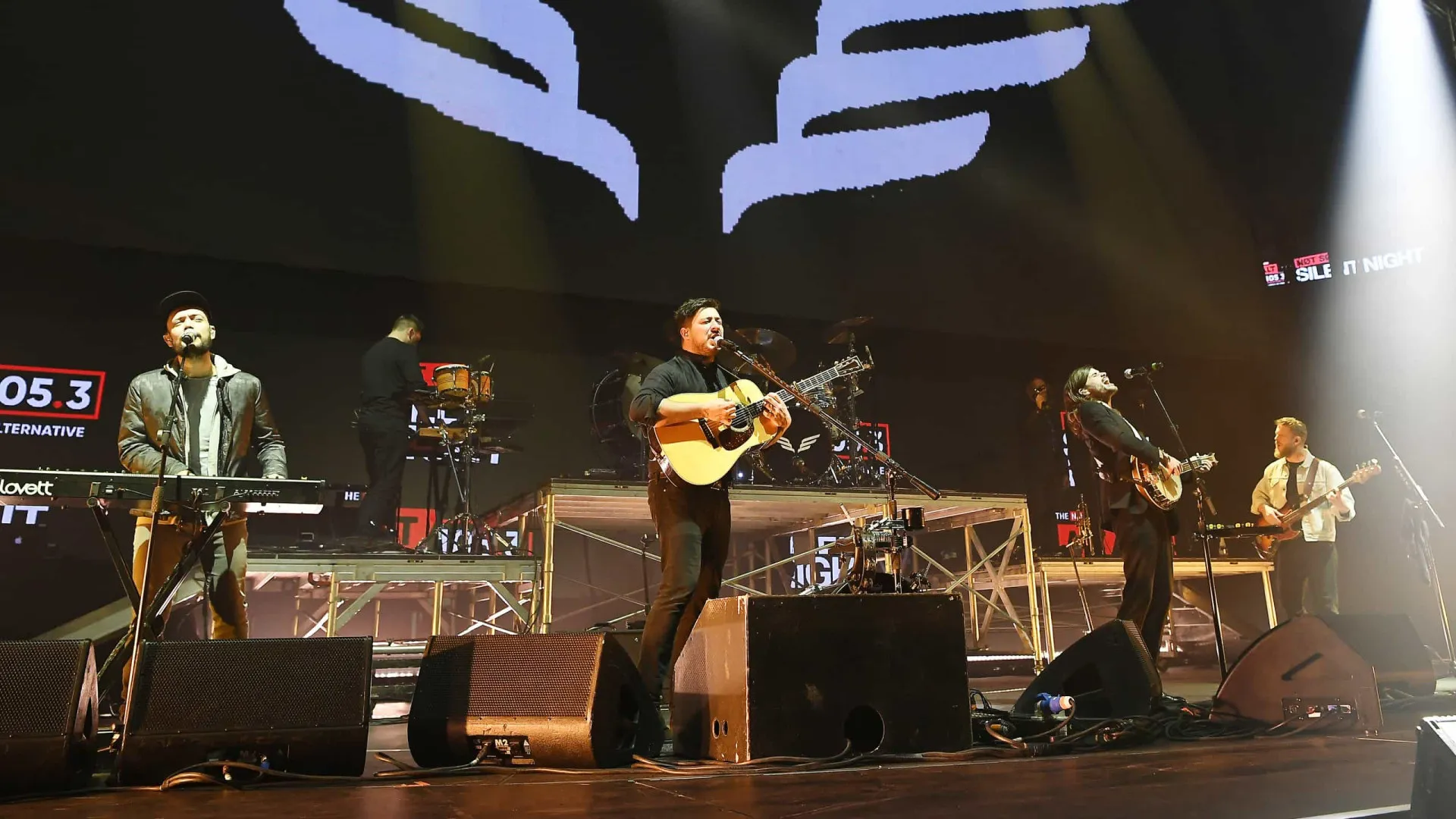 A banda Mumford & Sons em uma apresentação ao vivo, com seus instrumentos acústicos característicos.