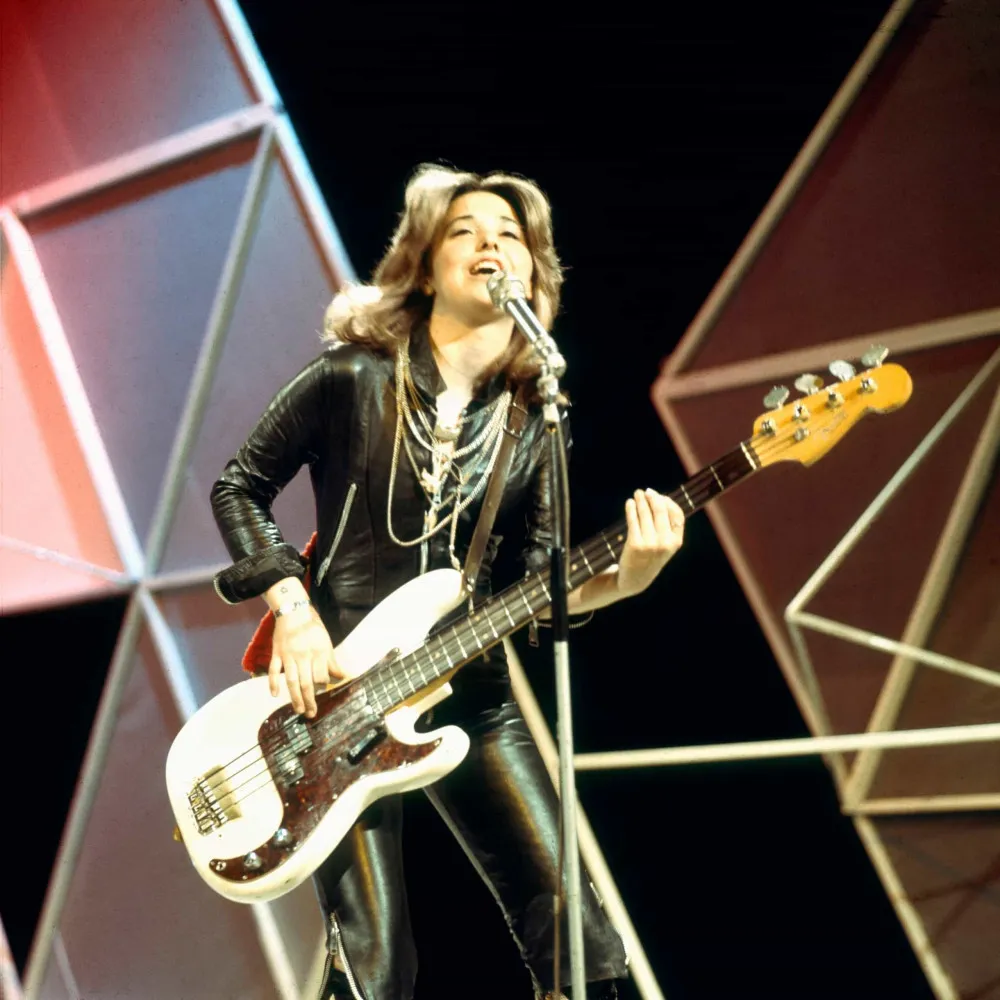 Suzi Quatro, pioneira do rock feminino, tocando baixo e cantando com energia.