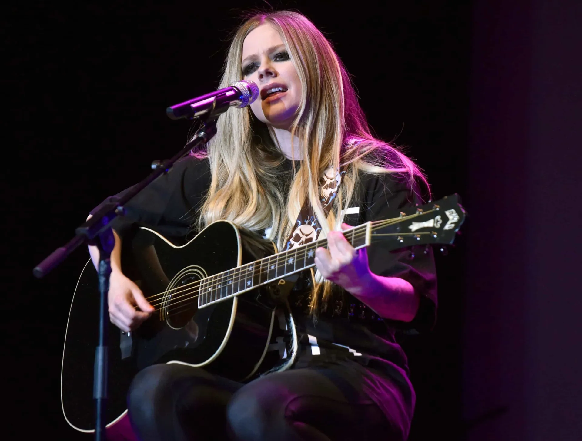 Avril Lavigne com um visual sombrio, usando um vestido preto e maquiagem escura.