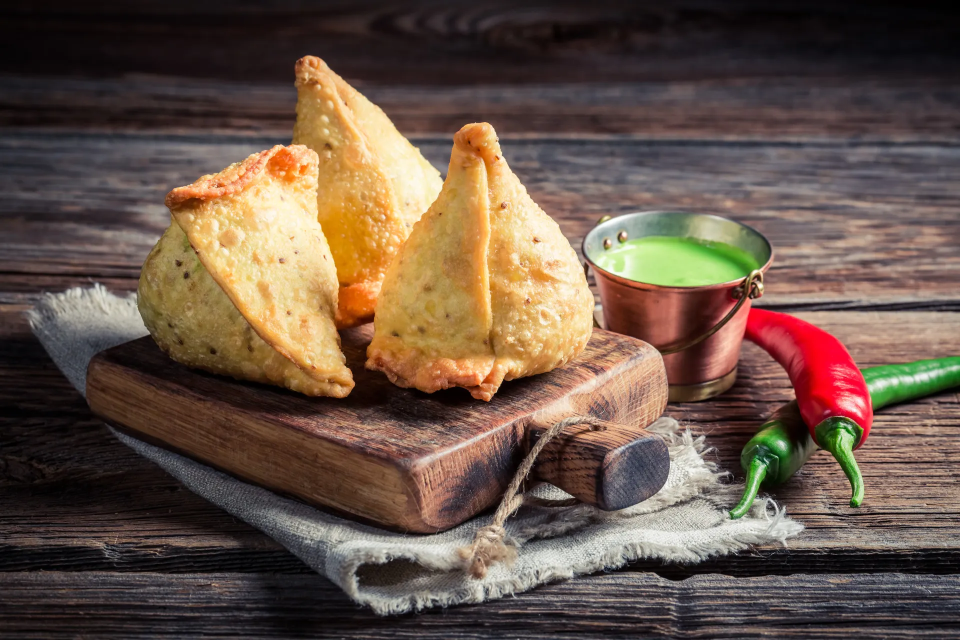 Chamuças (samosas) triangulares e douradas, servidas com molhos.