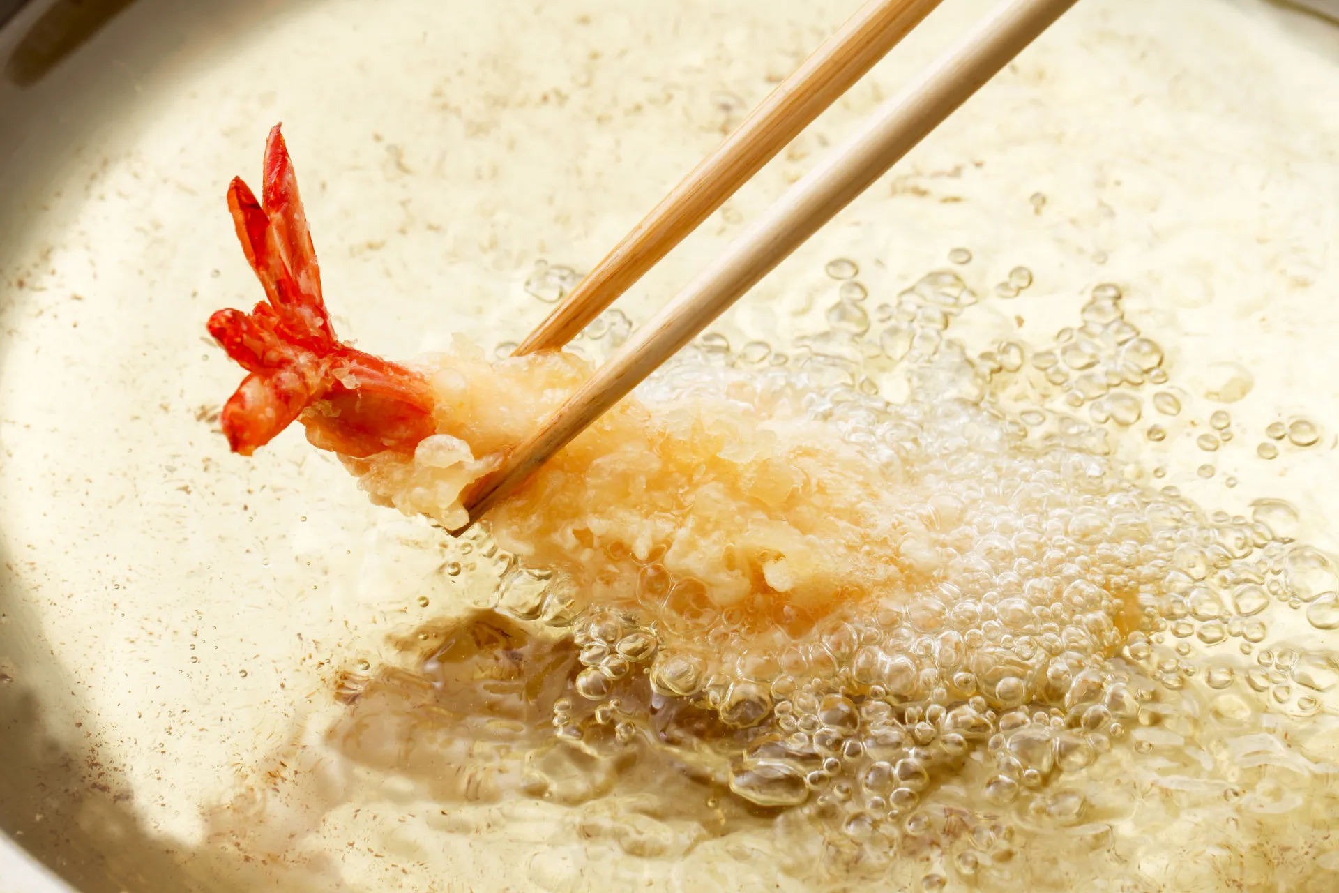 Close-up de um camarão empanado em tempura sendo mergulhado no molho.
