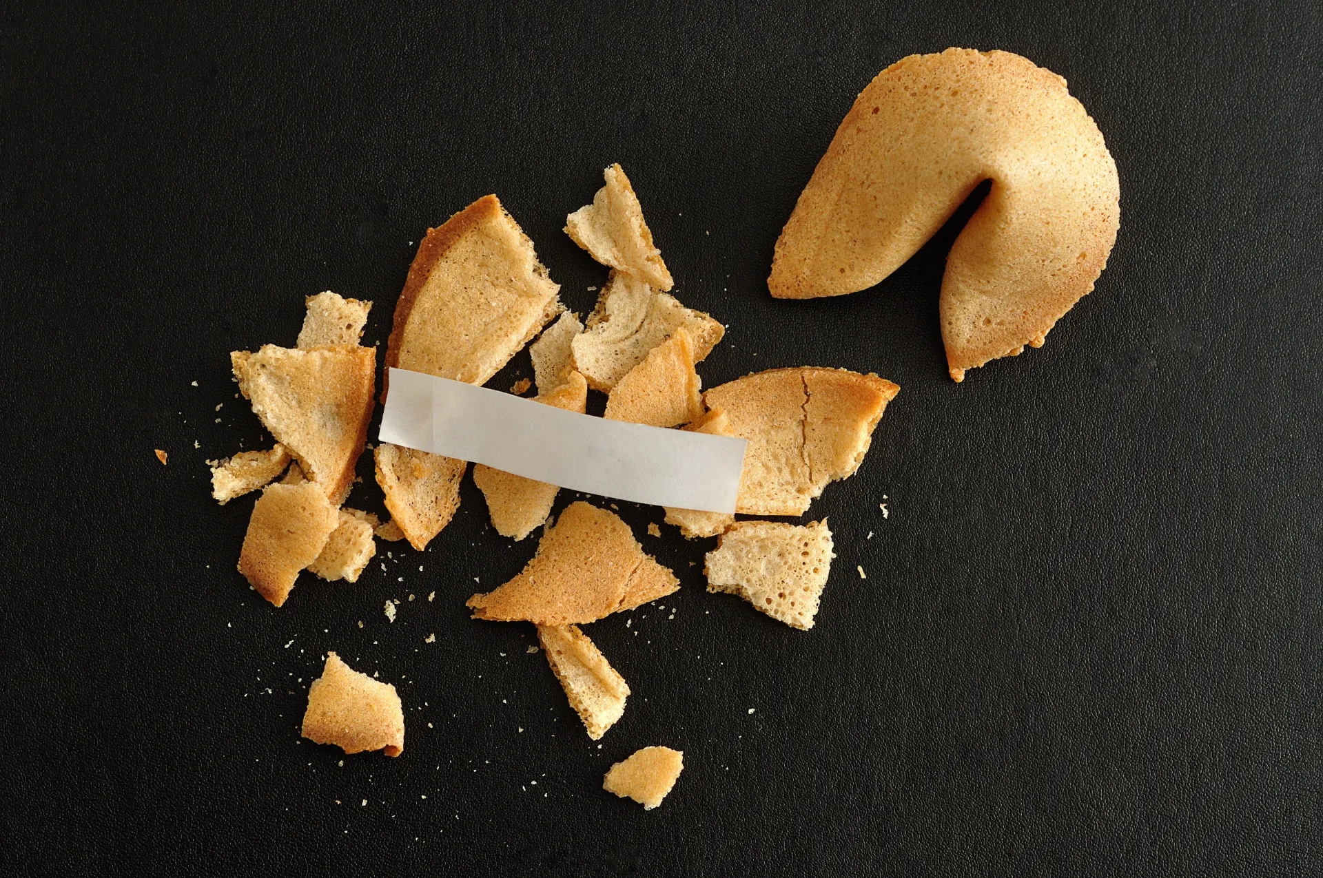 Mão segurando um biscoito da sorte quebrado, com a tira de papel com a mensagem à mostra.