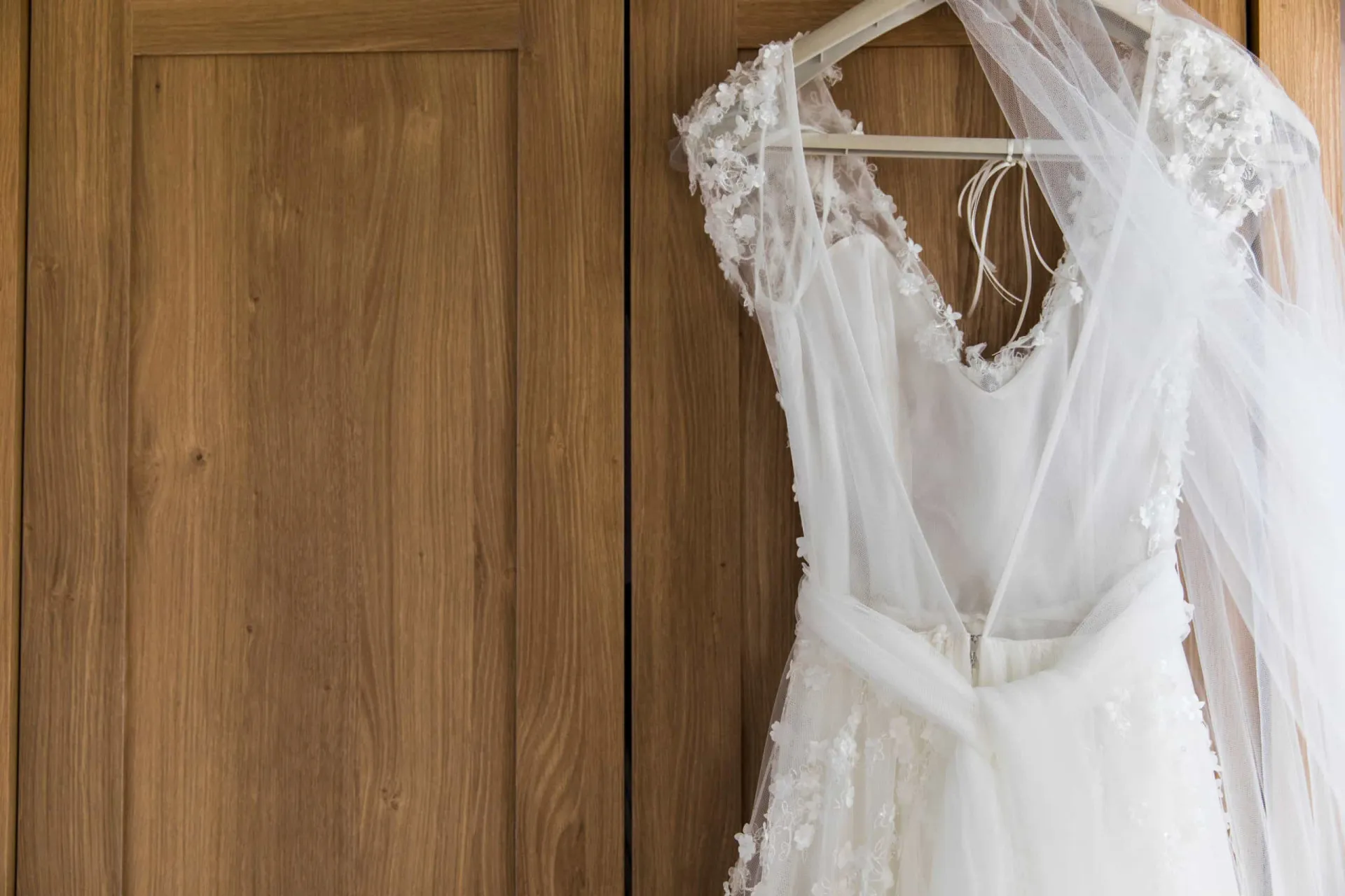 Noiva usando um vestido de casamento branco, olhando pela janela com um buquê nas mãos.