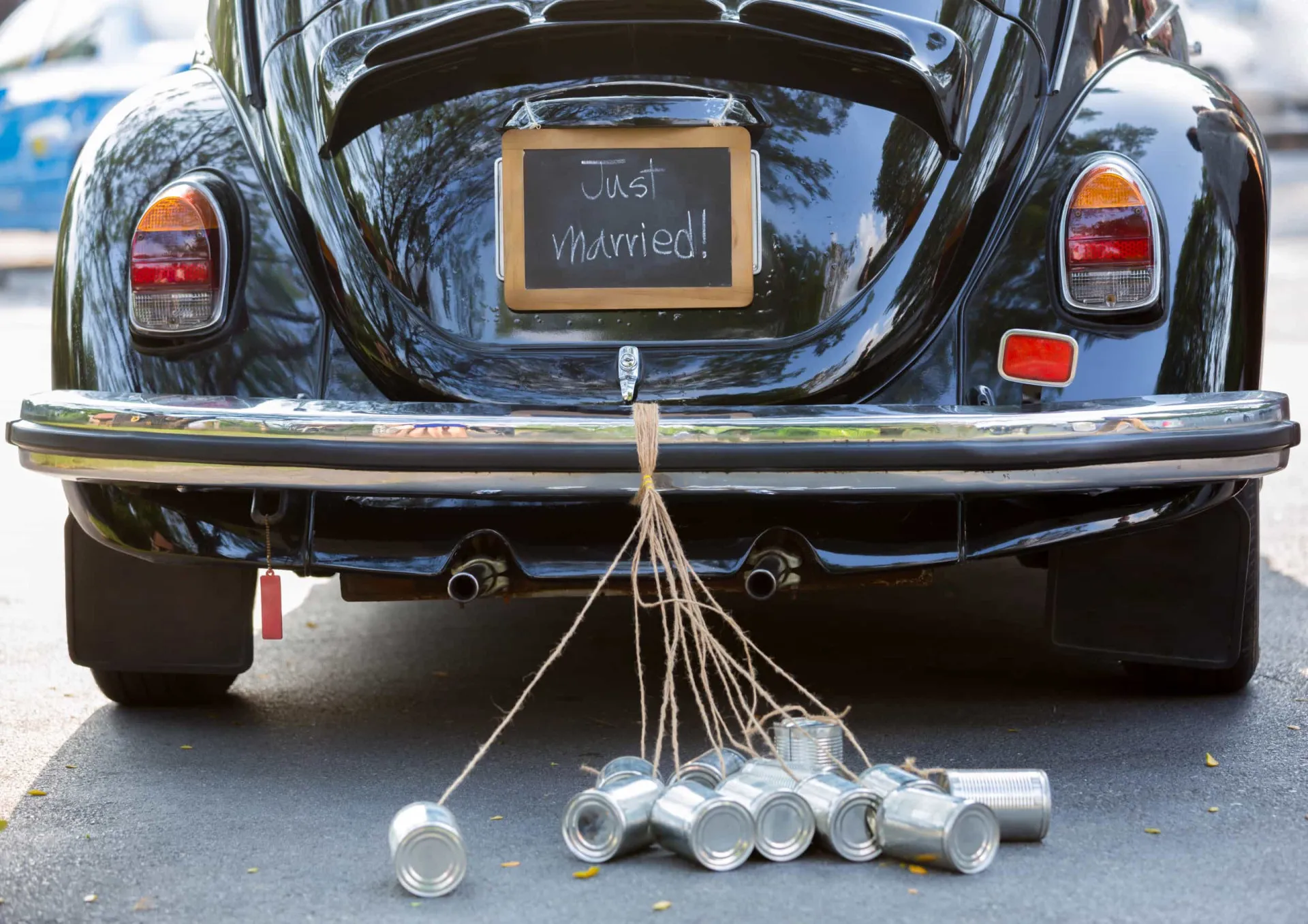 Carro de casamento decorado com latas amarradas no para-choque e uma placa de 'Recém-casados'.