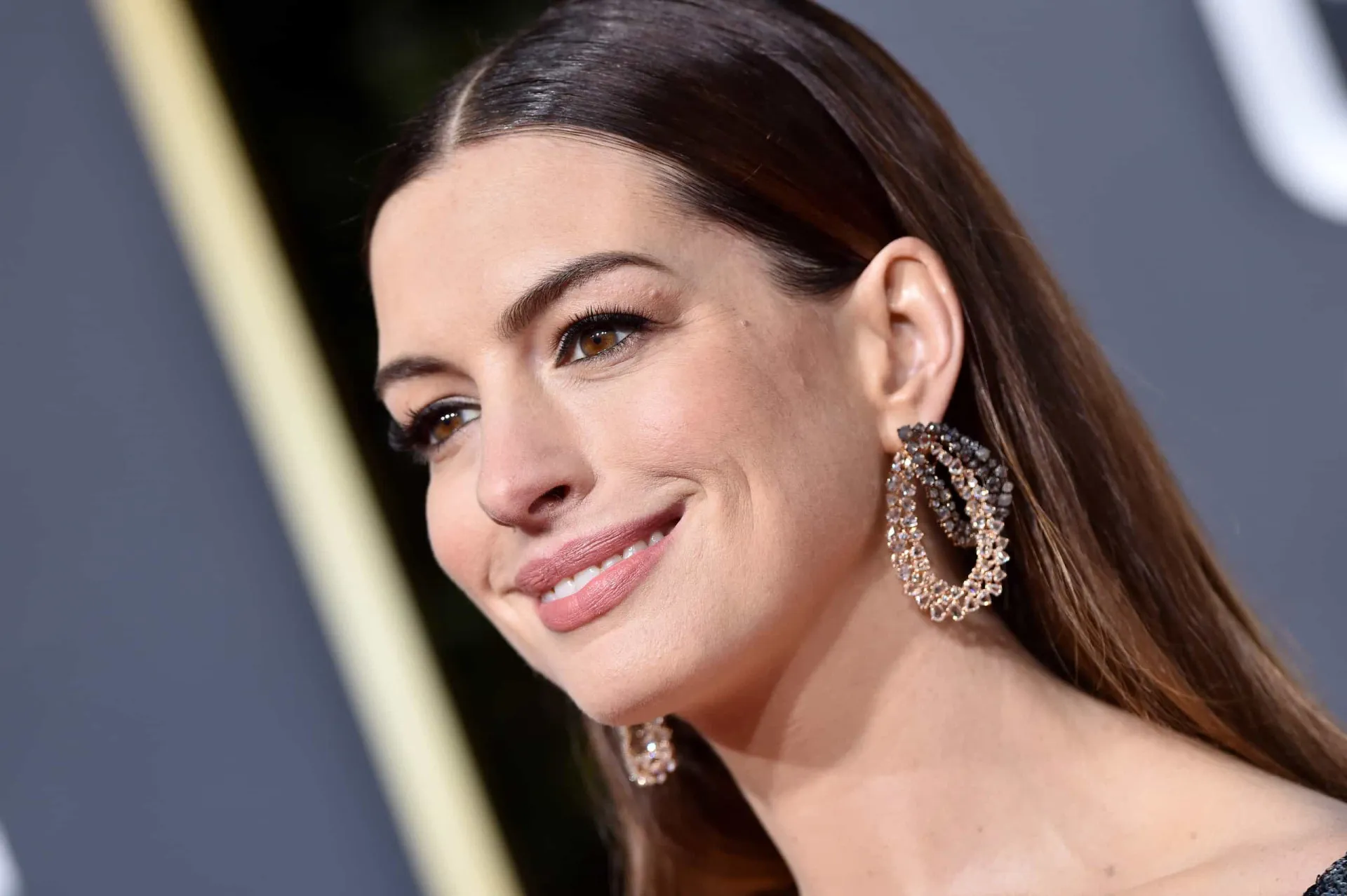Anne Hathaway em um evento, com olhar sério e cabelo curto.