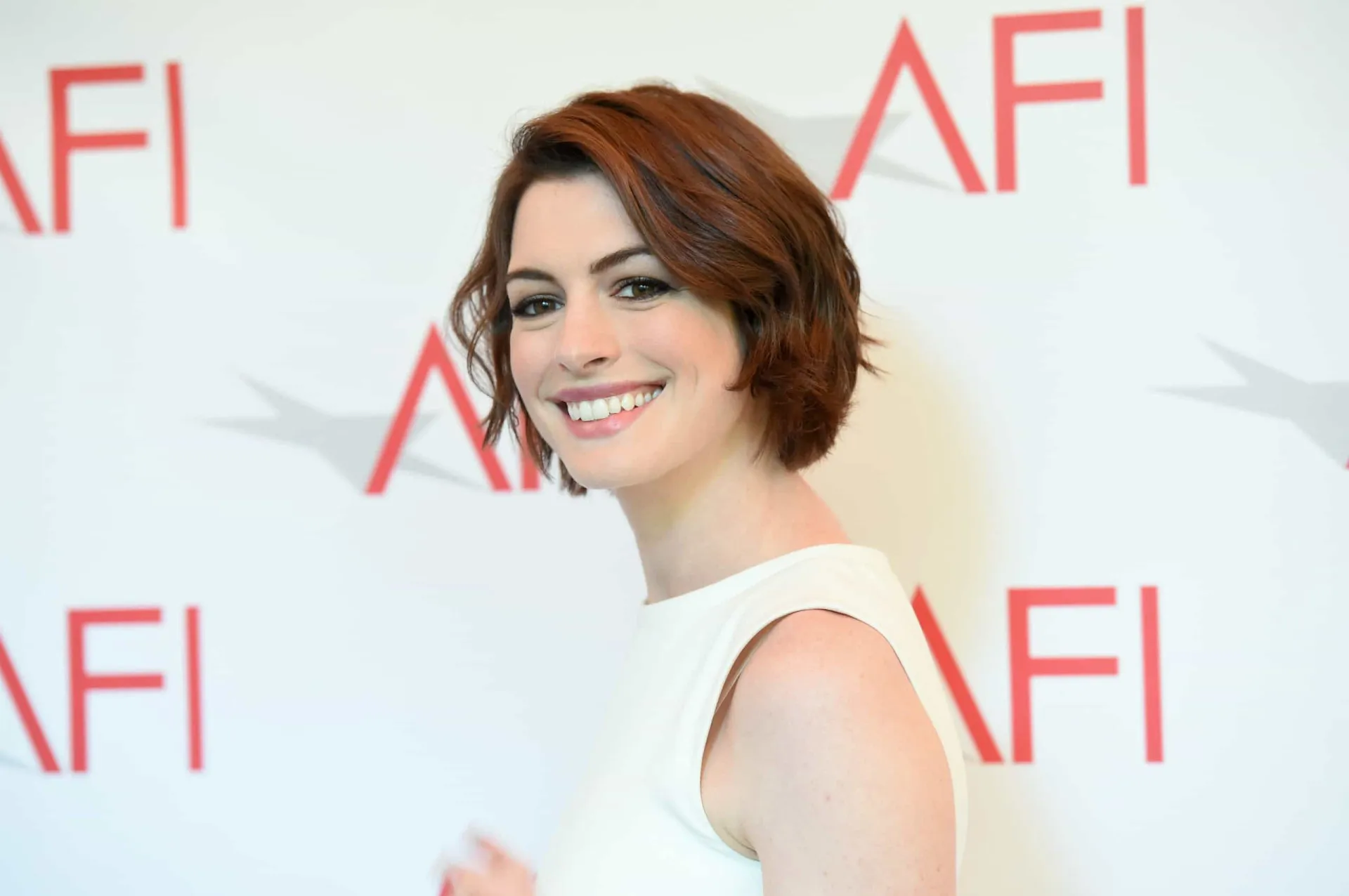 Anne Hathaway em um tapete vermelho, sorrindo para as câmeras.