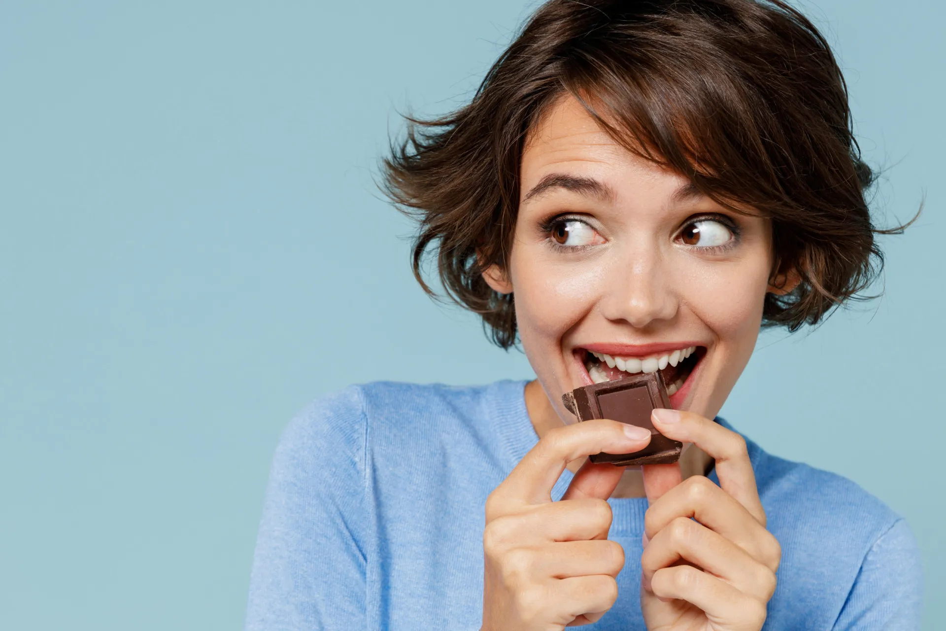 Mãos quebrando uma barra de chocolate amargo com a porcentagem de cacau visível na embalagem.