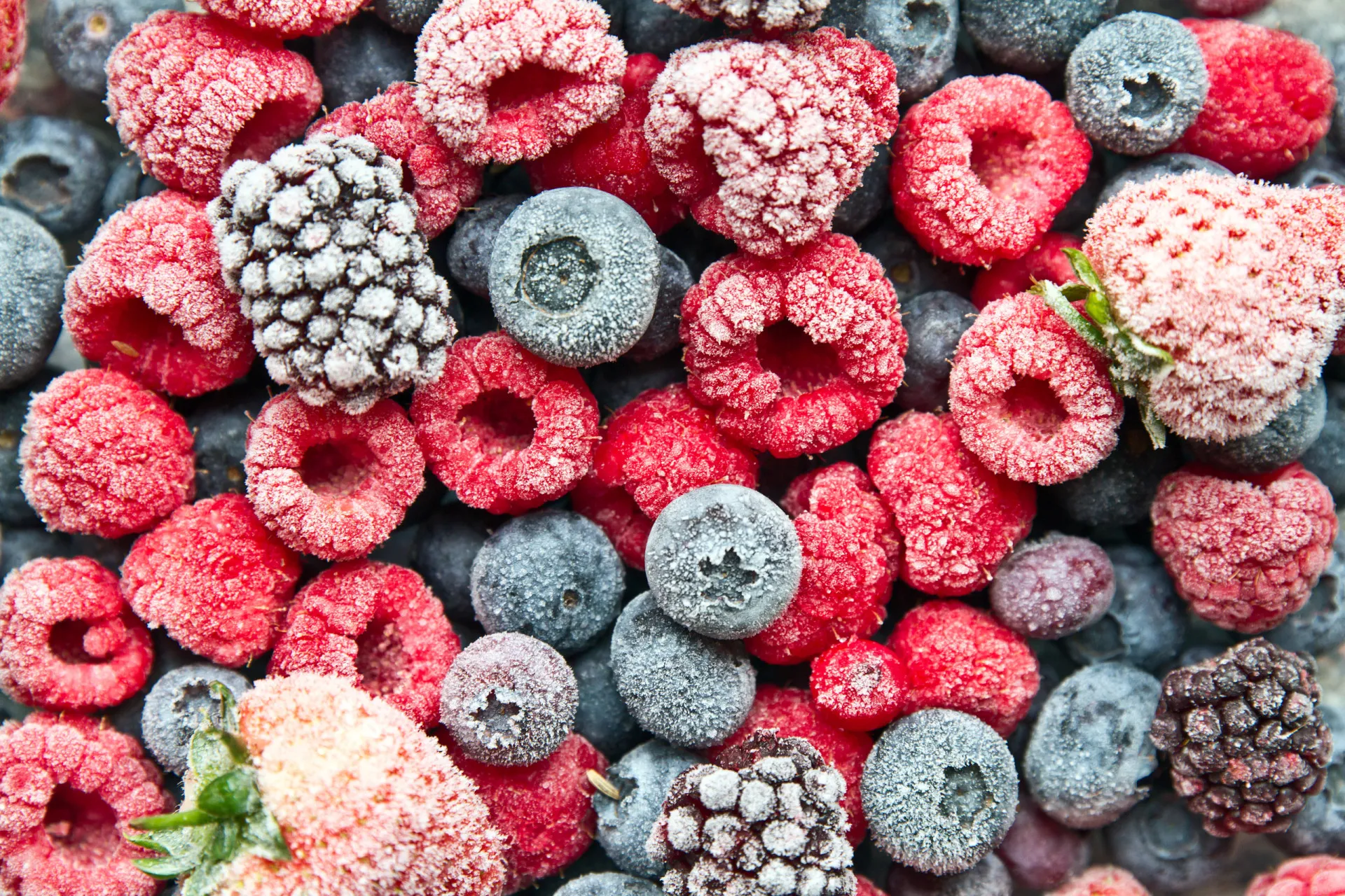 Variedade de vegetais e frutas congelados, como brócolis, ervilhas e morangos.