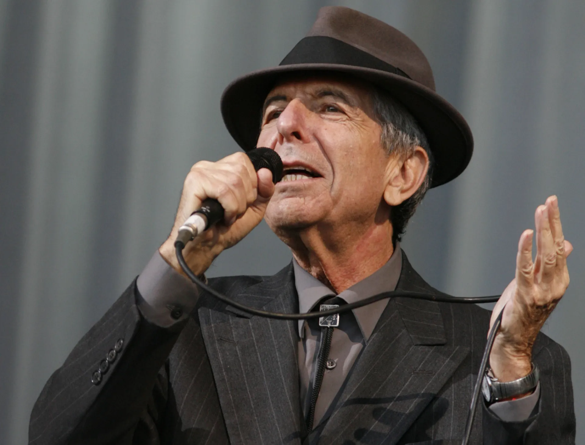 O lendário Leonard Cohen em uma performance, com seu chapéu característico e um olhar profundo.