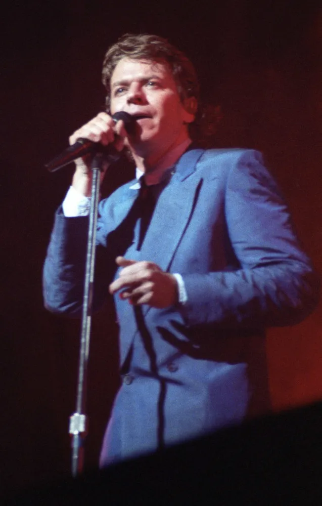 O cantor Robert Palmer, elegantemente vestido, em uma performance durante os anos 80.