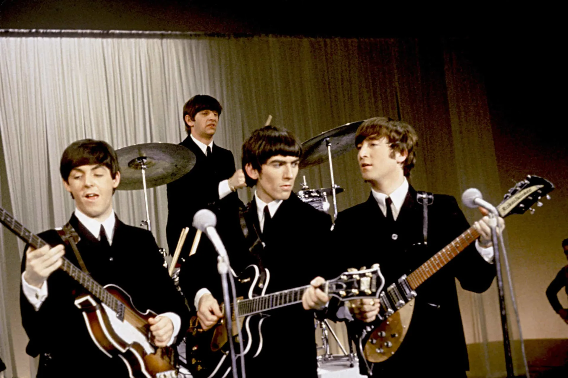 Os Beatles em uma sessão de fotos promocional, vestidos com ternos elegantes, no auge da fama.