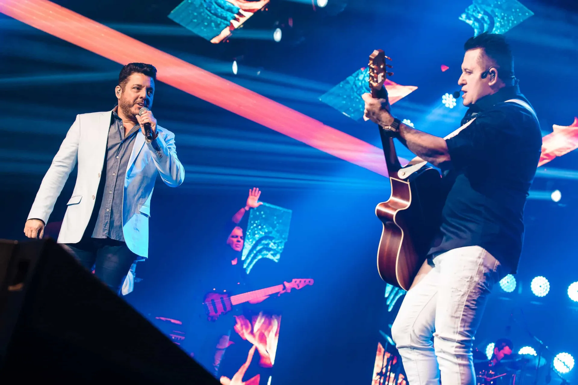 A dupla sertaneja Bruno e Marrone se apresentando em um palco, com luzes coloridas.