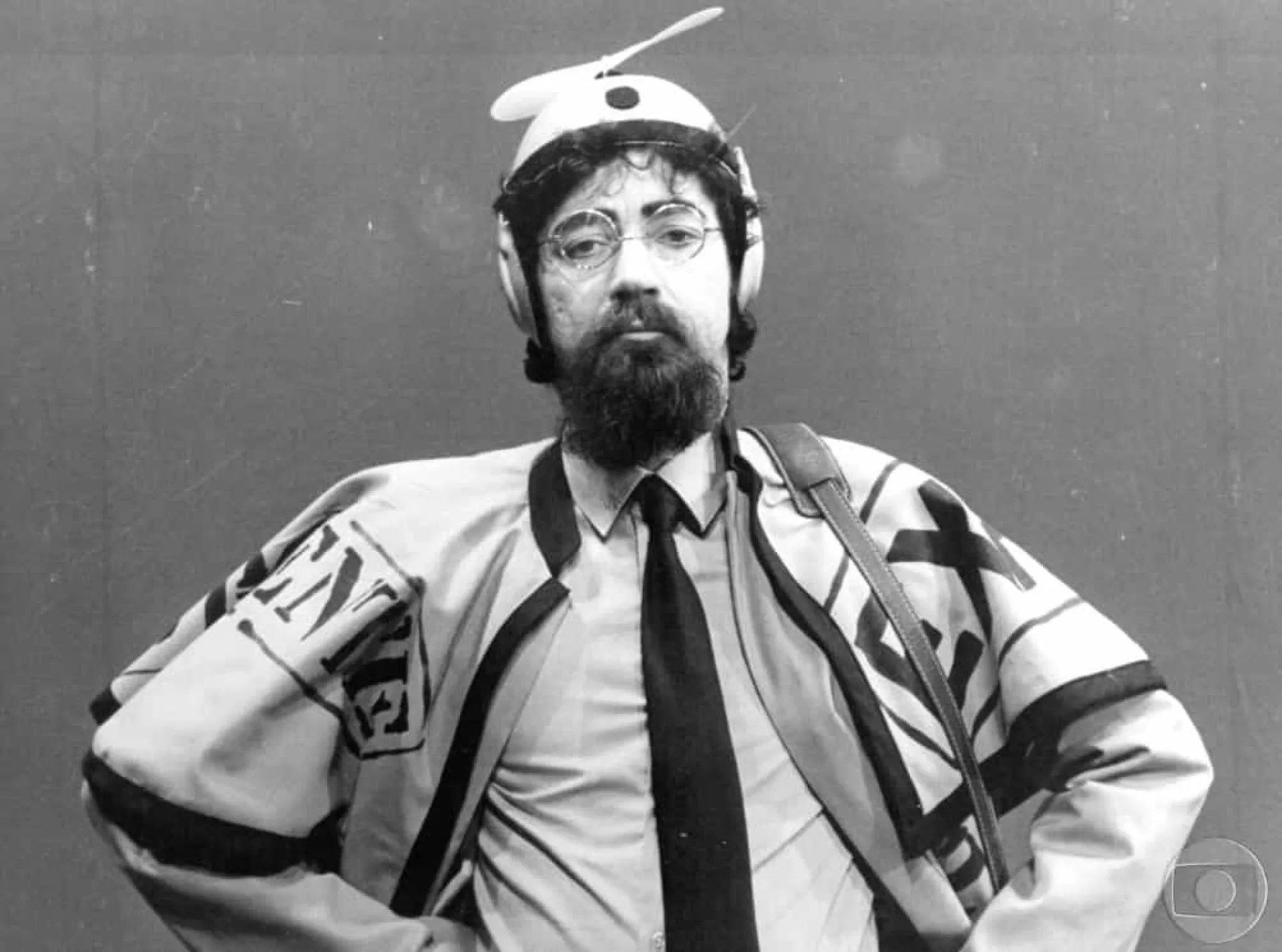 Raul Seixas em uma pose icônica, com óculos escuros e cabelos longos, durante uma apresentação.