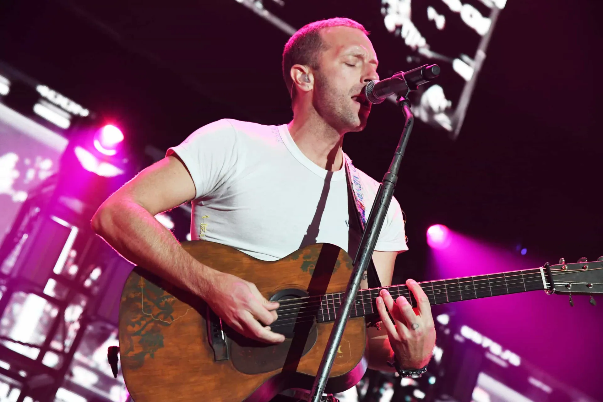 Chris Martin, vocalista do Coldplay, tocando piano durante um show, com luzes azuis ao fundo.