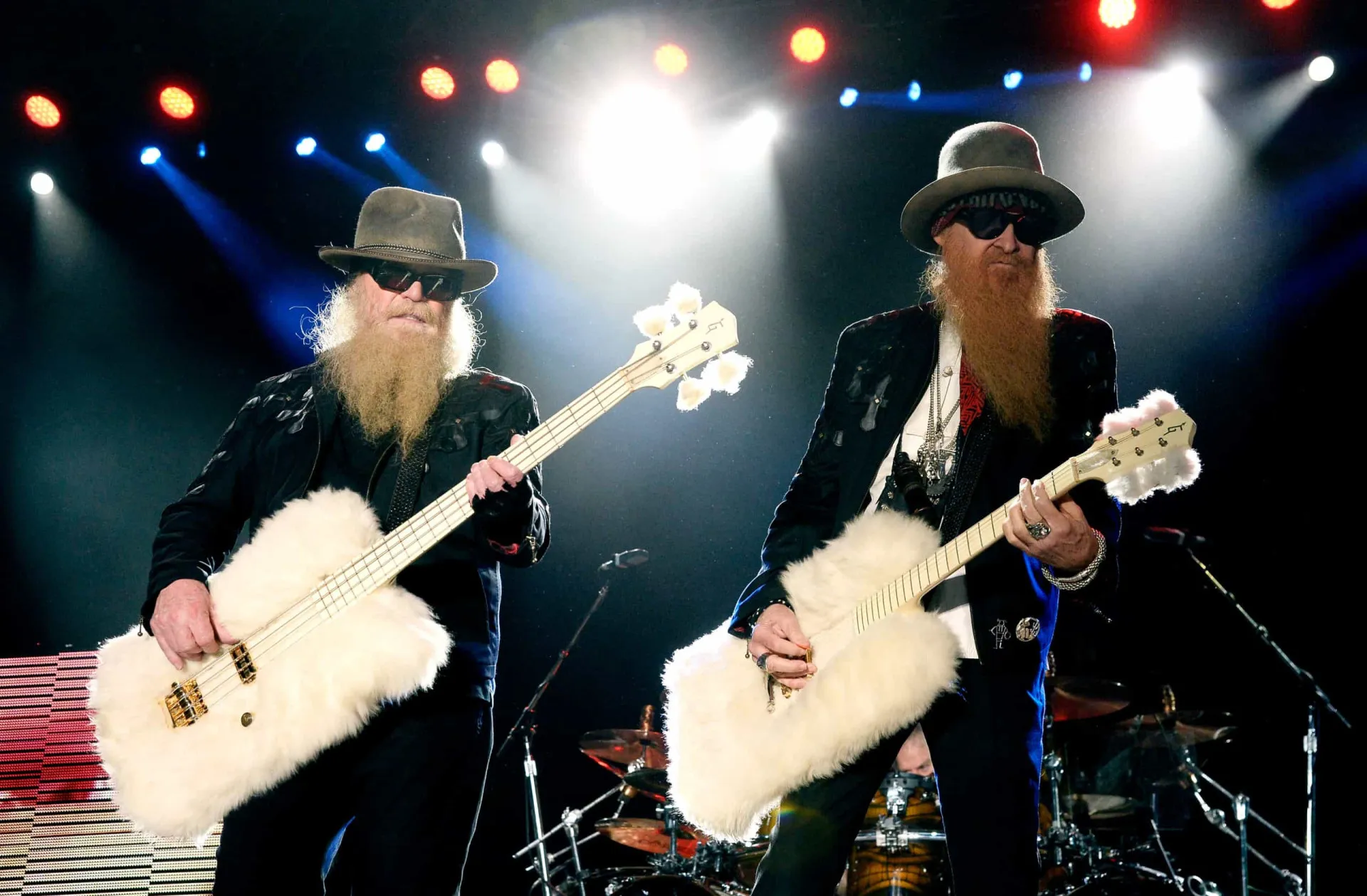 A banda ZZ Top com suas longas barbas e óculos escuros, posando ao lado de um carro clássico.
