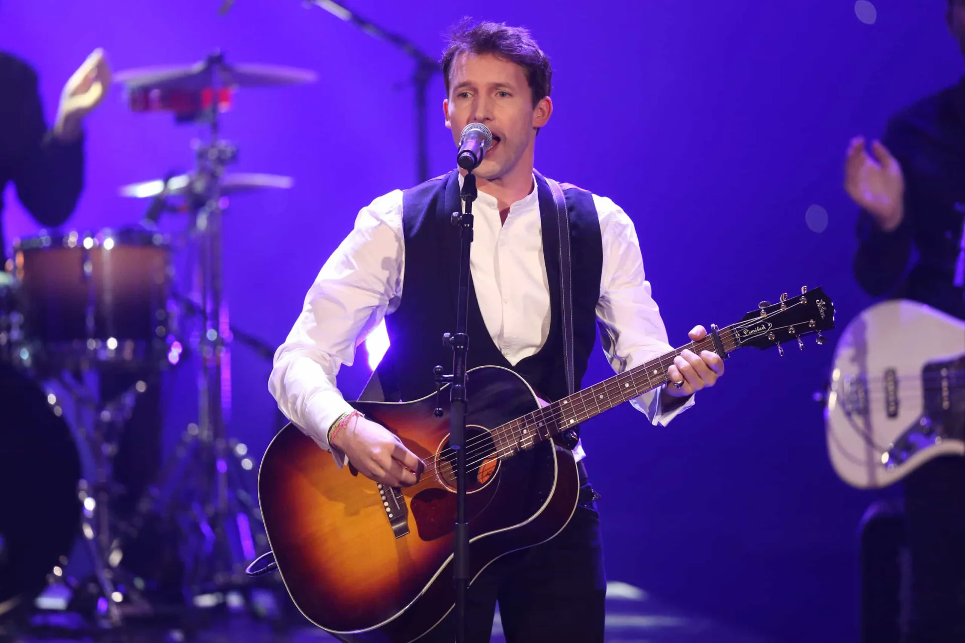 James Blunt cantando e tocando violão durante um show, com uma expressão concentrada.