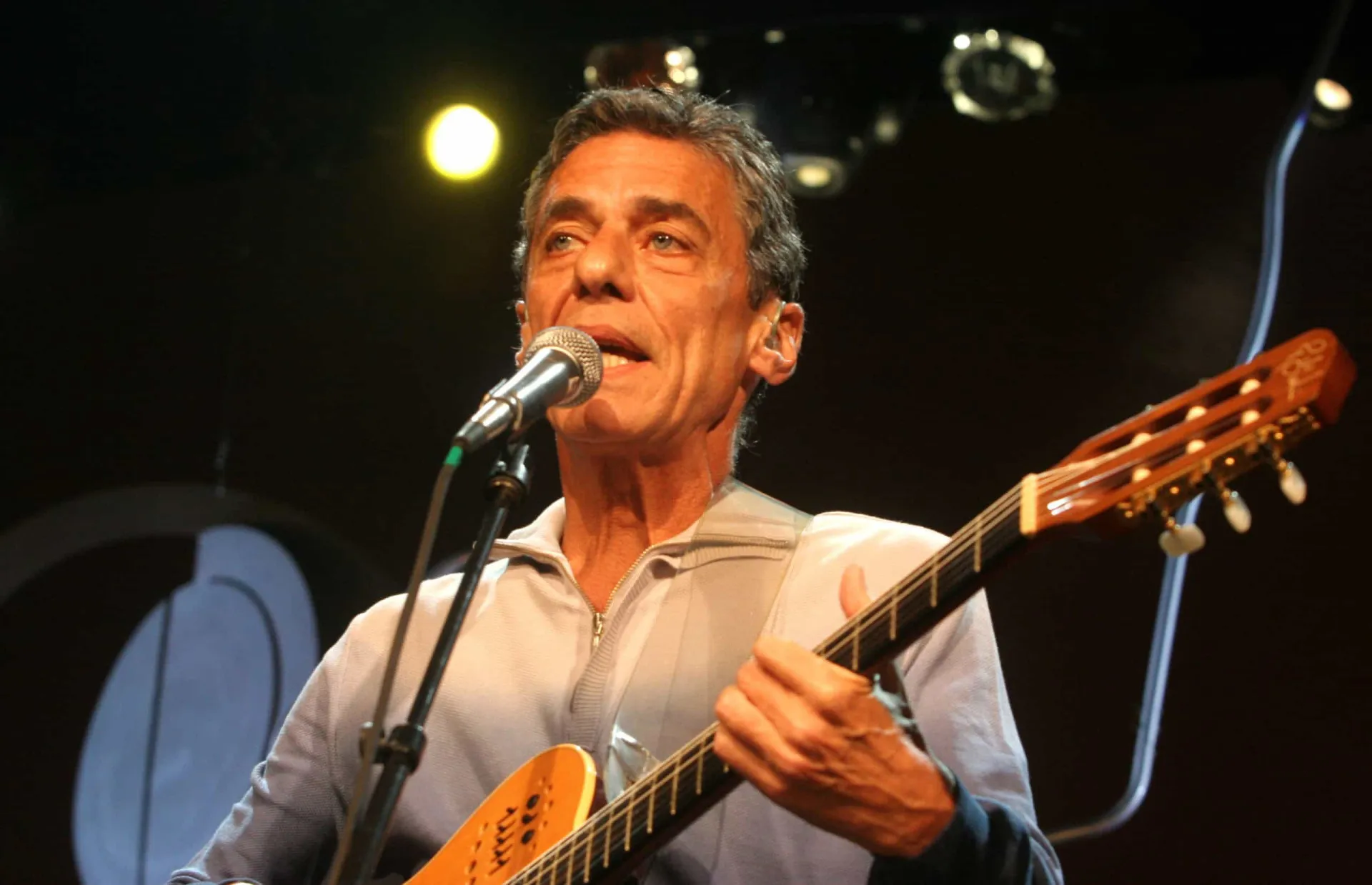 Chico Buarque cantando em um show, com seu violão e um olhar concentrado.