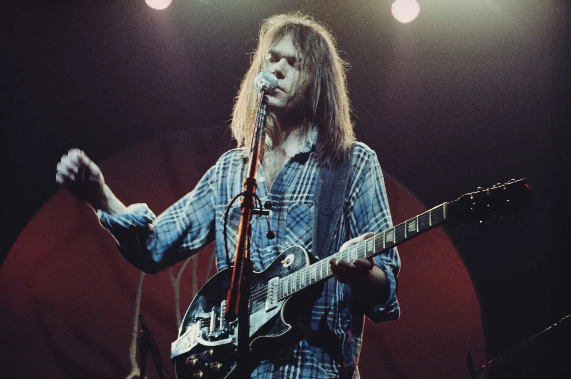 Neil Young tocando seu violão e gaita em uma performance solo e intimista.