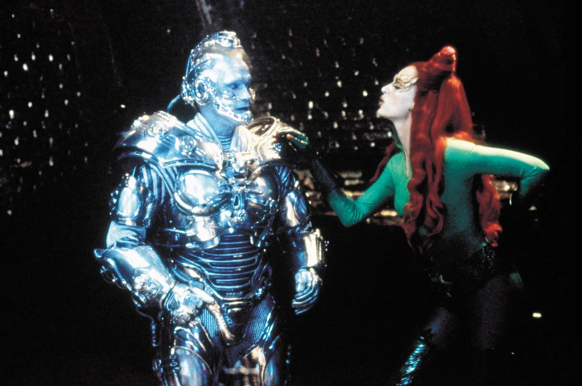 Joel Schumacher no set de filmagem, gesticulando enquanto dirige uma cena, visivelmente engajado no processo.