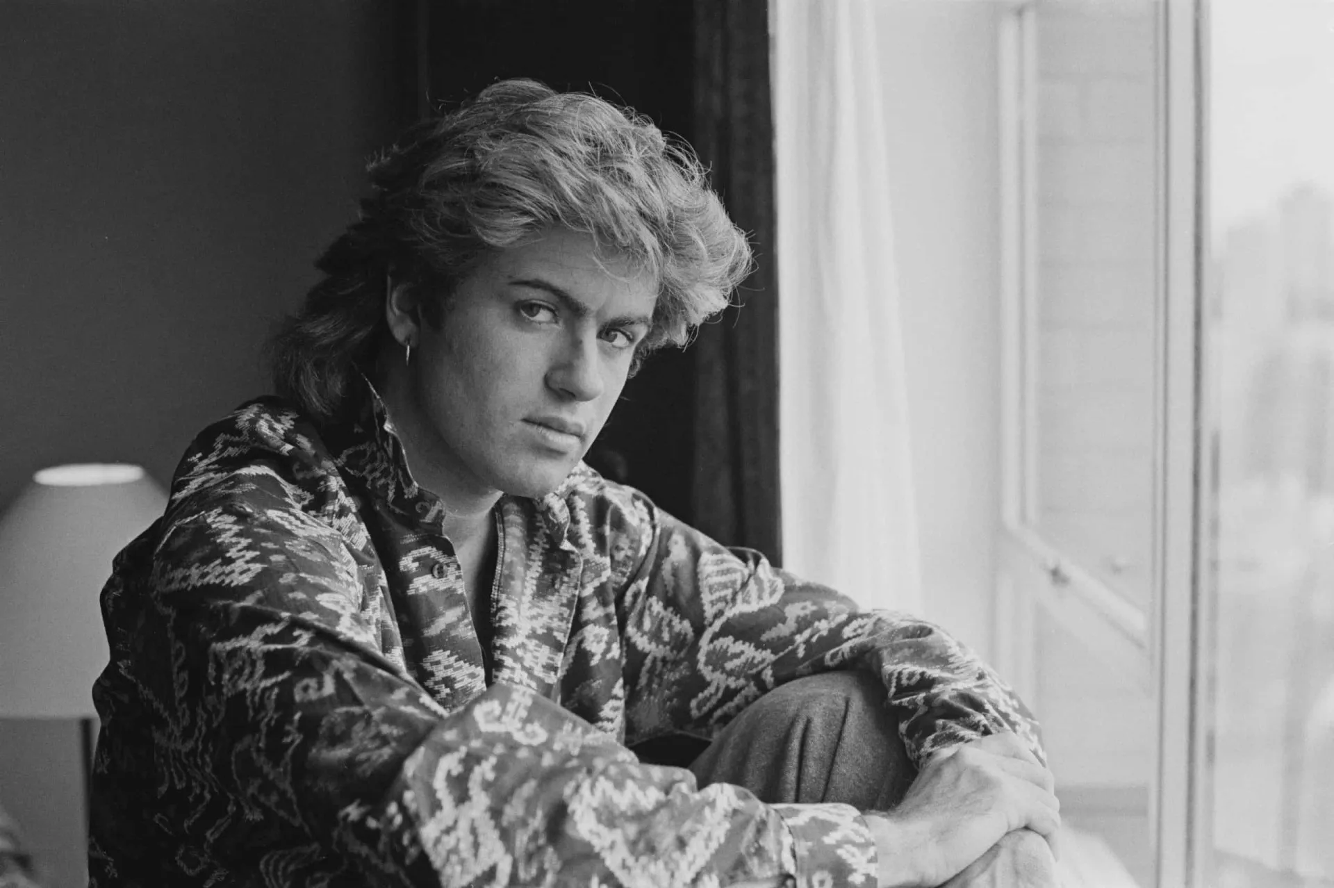 George Michael com seu icônico visual dos anos 80, incluindo o brinco de cruz.