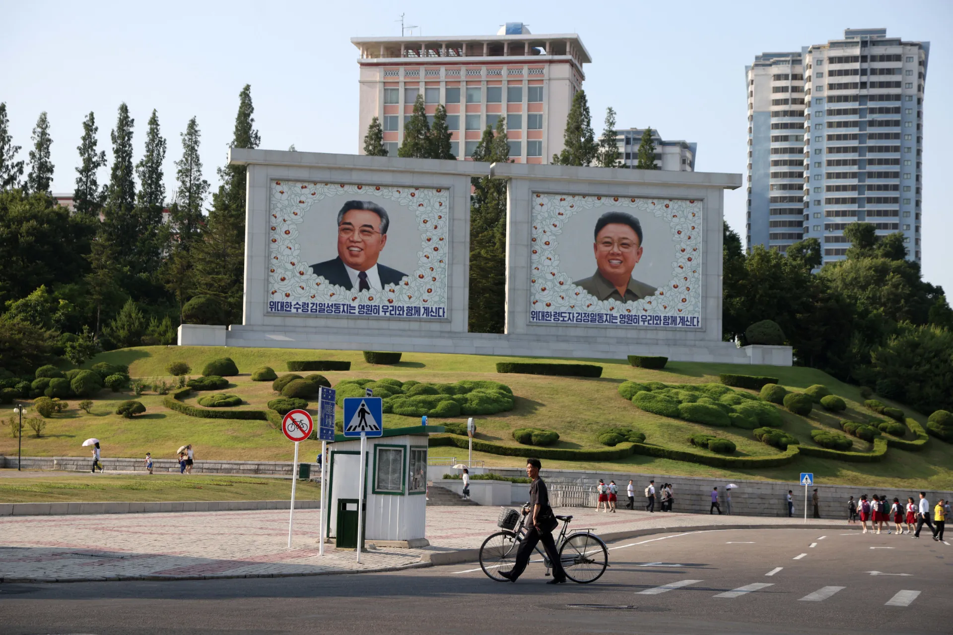 Moradores de Pyongyang passando por outdoors gigantes com os retratos de Kim Il Sung e Kim Jong Il.