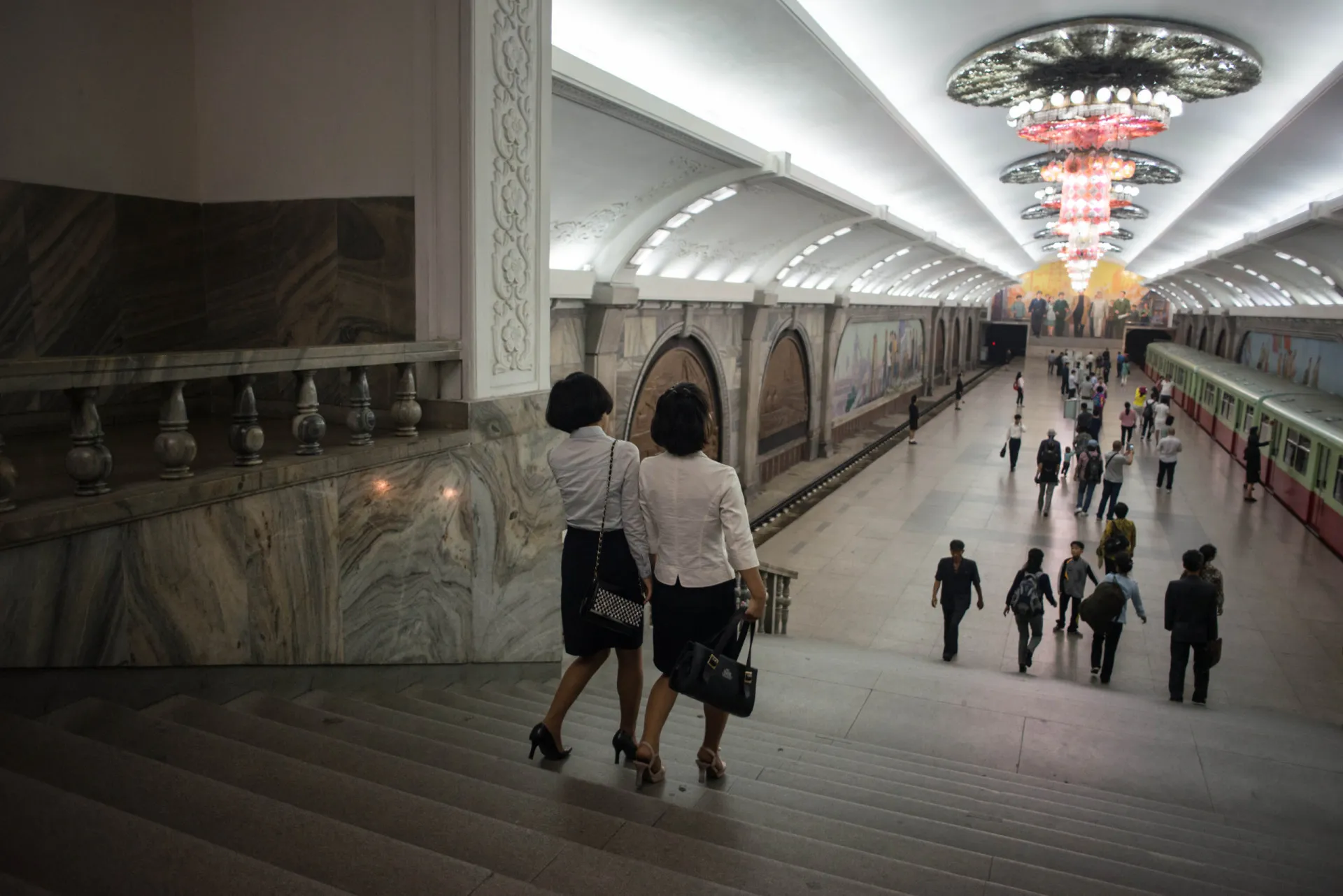 Passageiros descendo uma escada rolante em direção a uma plataforma do metrô de Pyongyang.