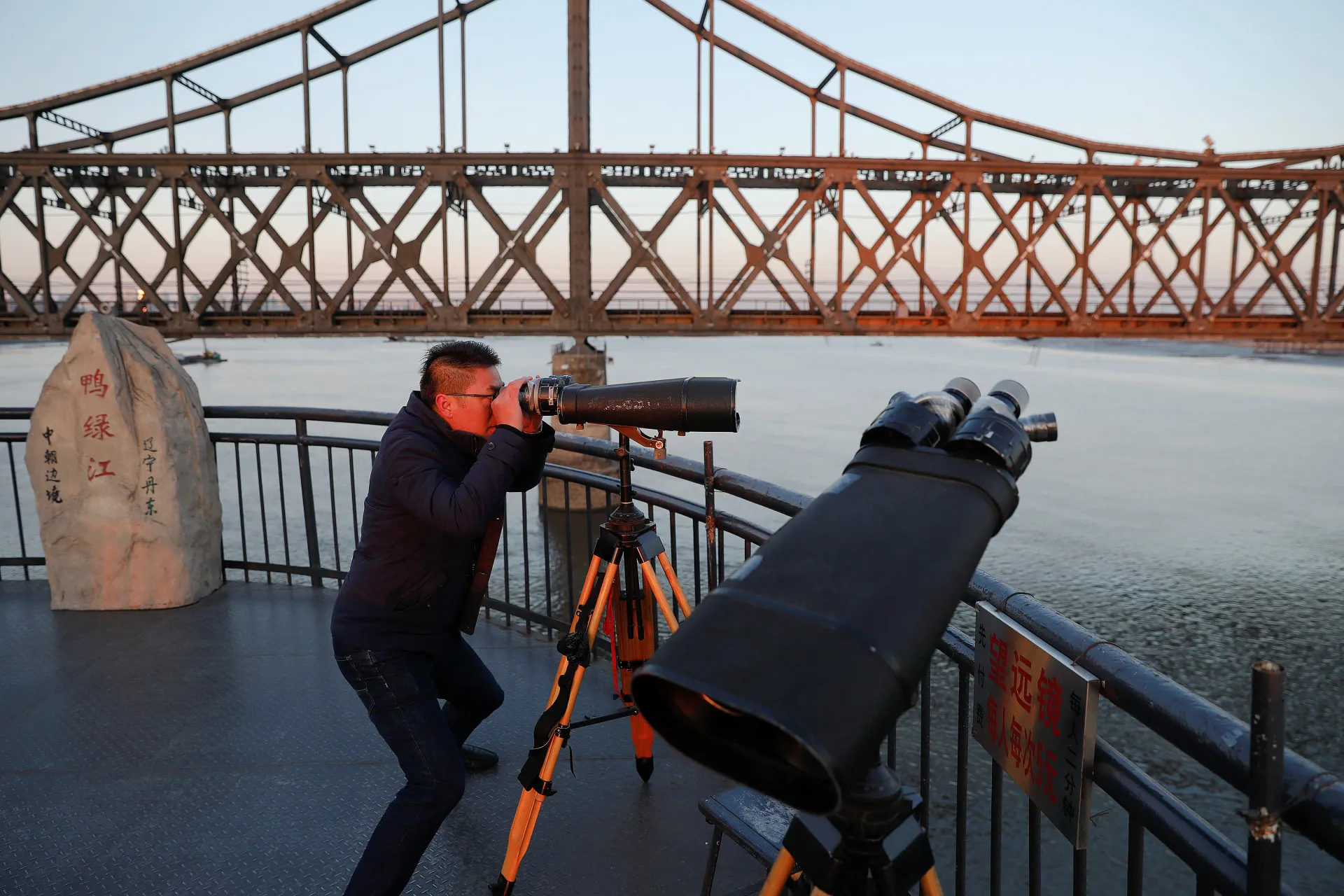 Cidadão chinês olhando intensamente para a Coreia do Norte através de binóculos.